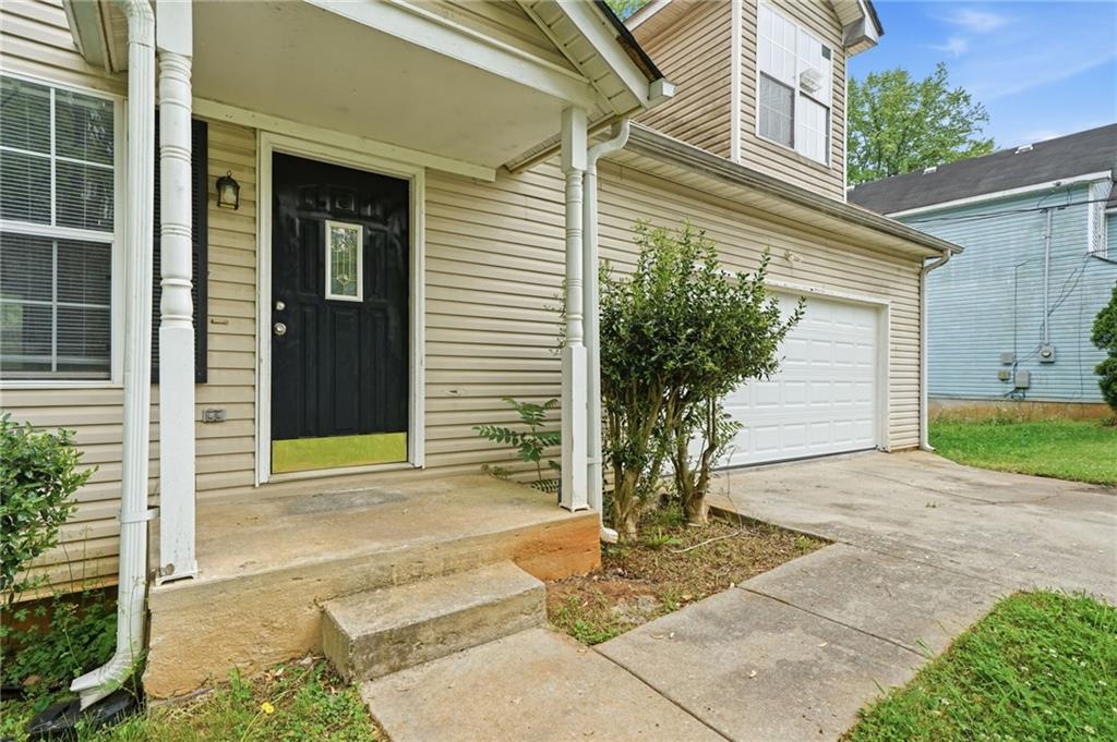 Beige two-story house with a covered porch, black front door, and white double garage door.