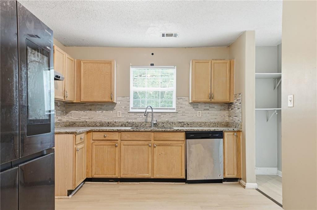 Kitchen with light wood cabinets, granite counters, tiled backsplash, and a window above the sink.