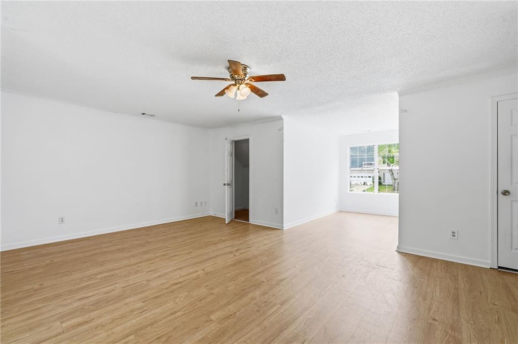 Vacant living room with wood-look floors, a ceiling fan, and a sunlit window.