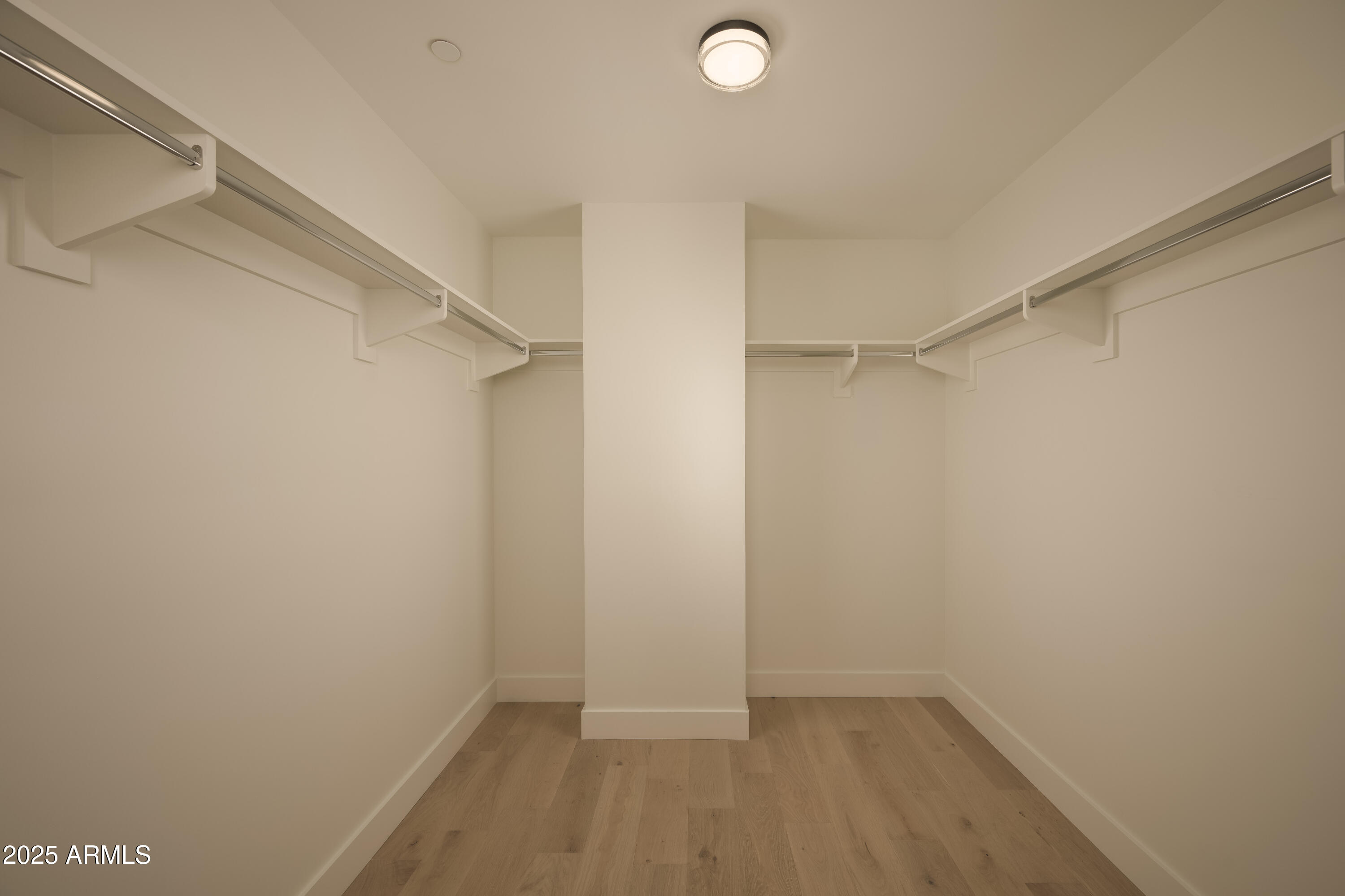 Empty walk-in closet with wood flooring and hanging rods along three walls.