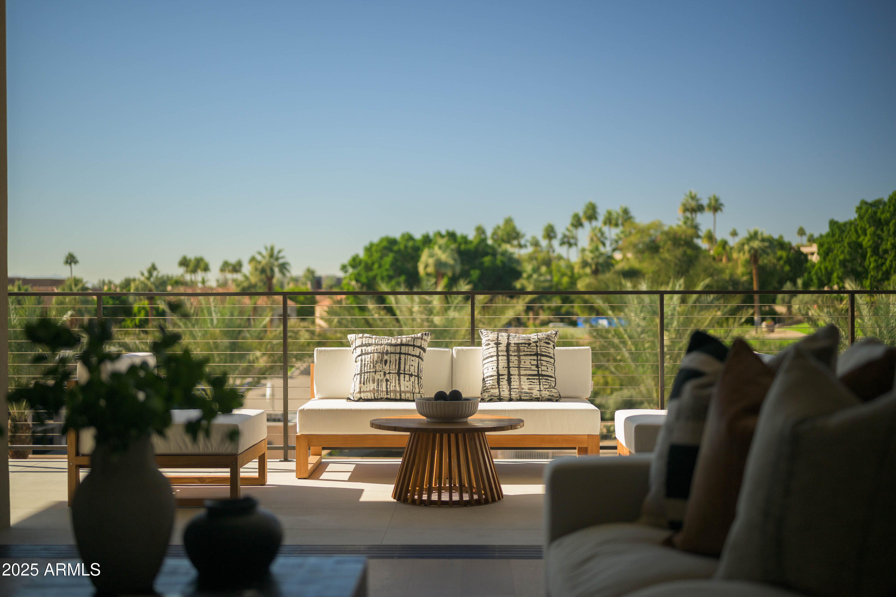 Outdoor terrace with white seating and a view of palm trees and greenery.