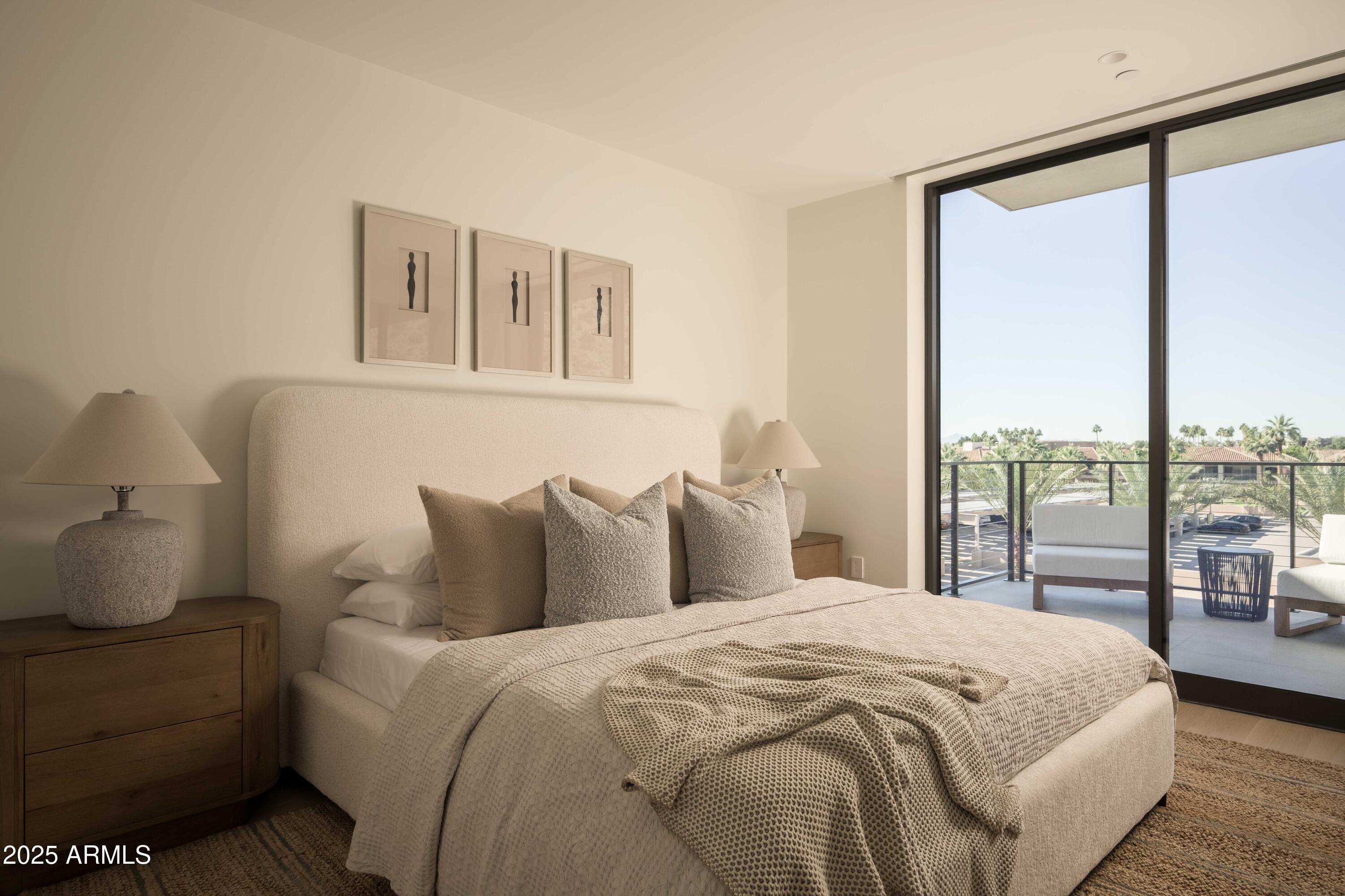 Staged bedroom with a cream upholstered bed and sliding glass doors opening to a palm-lined balcony.