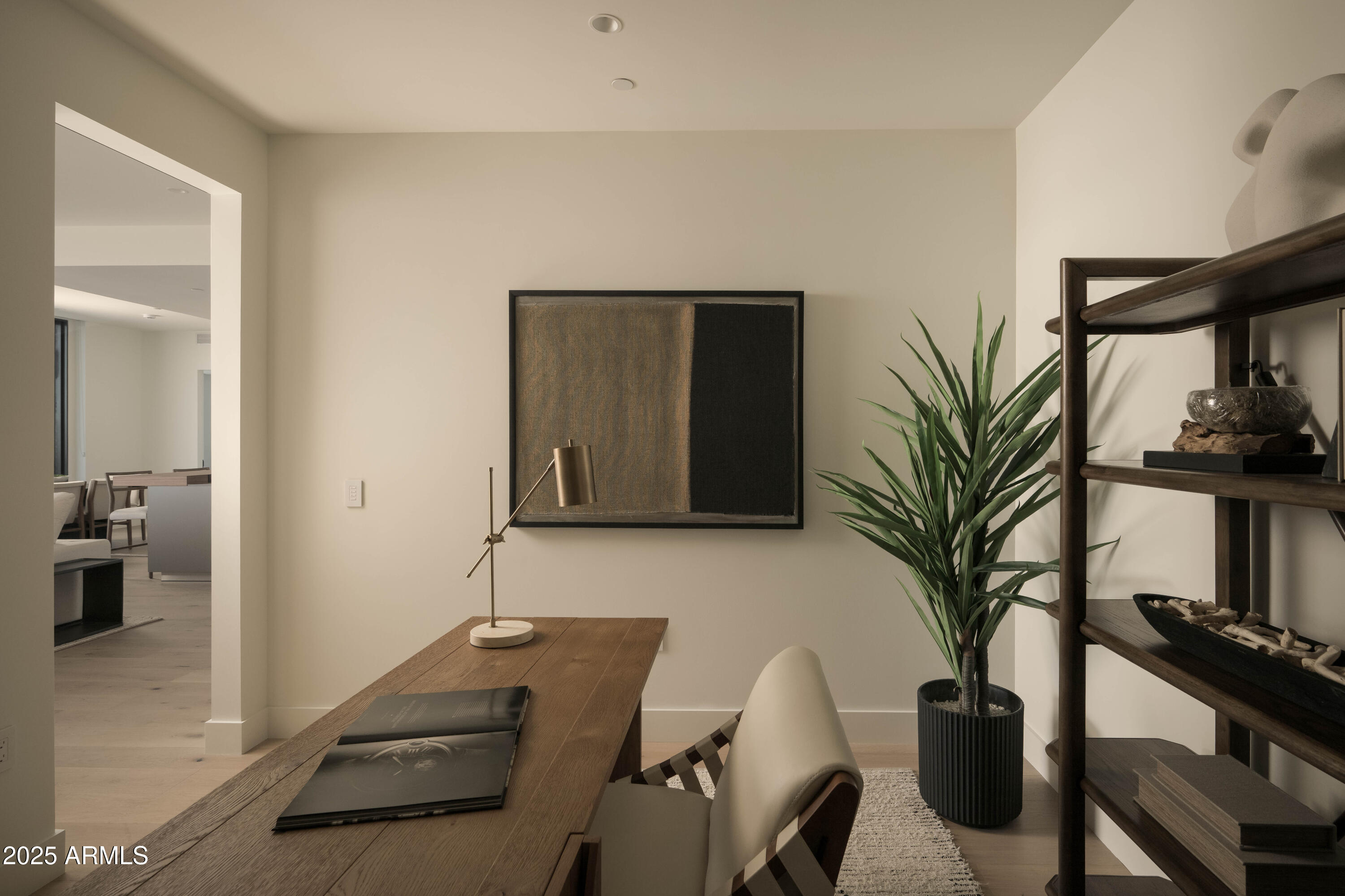Home office with a wooden desk, brass lamp, potted plant, and dark open shelving.