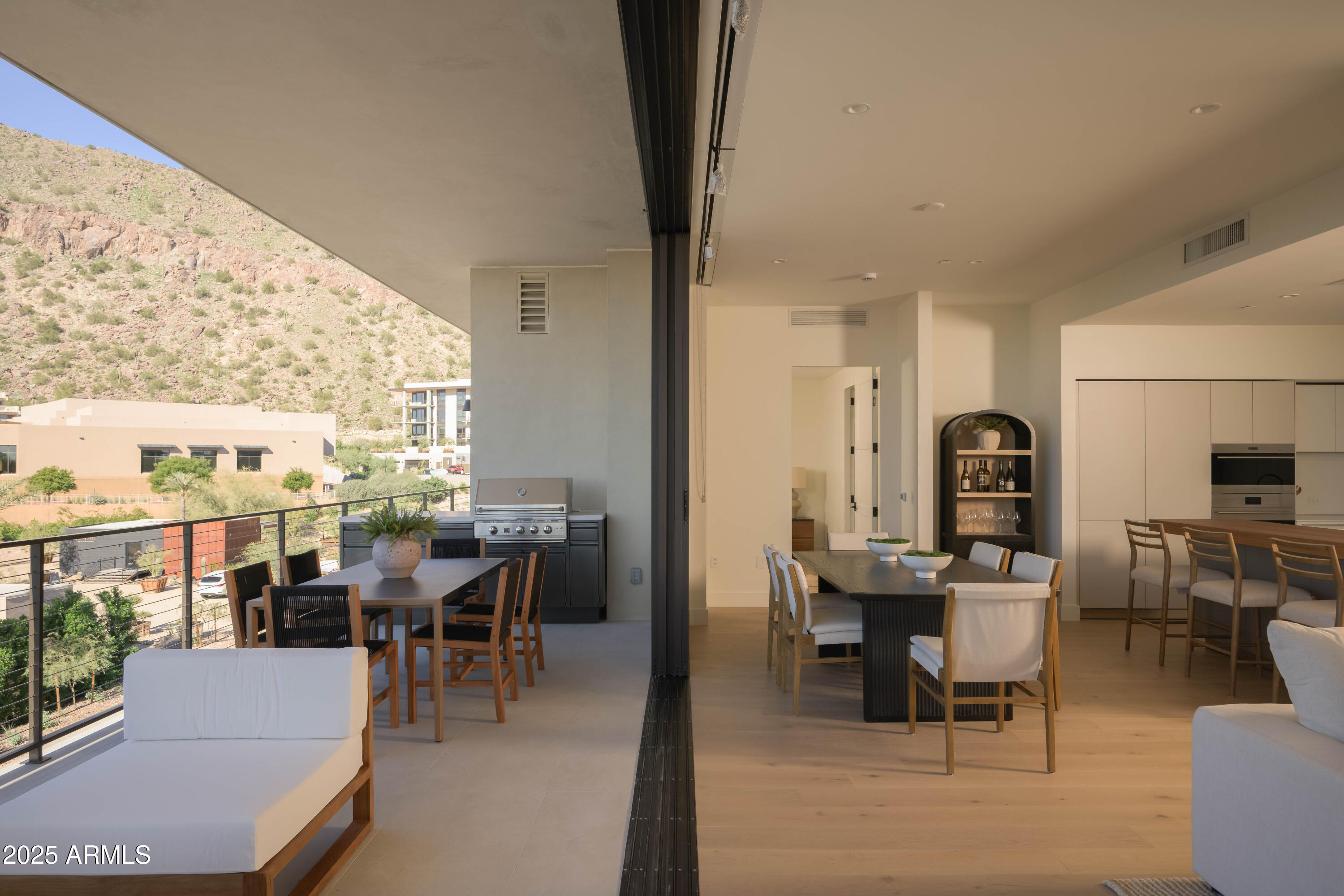 Open dining room and kitchen connect to a furnished balcony overlooking a rocky desert hillside.