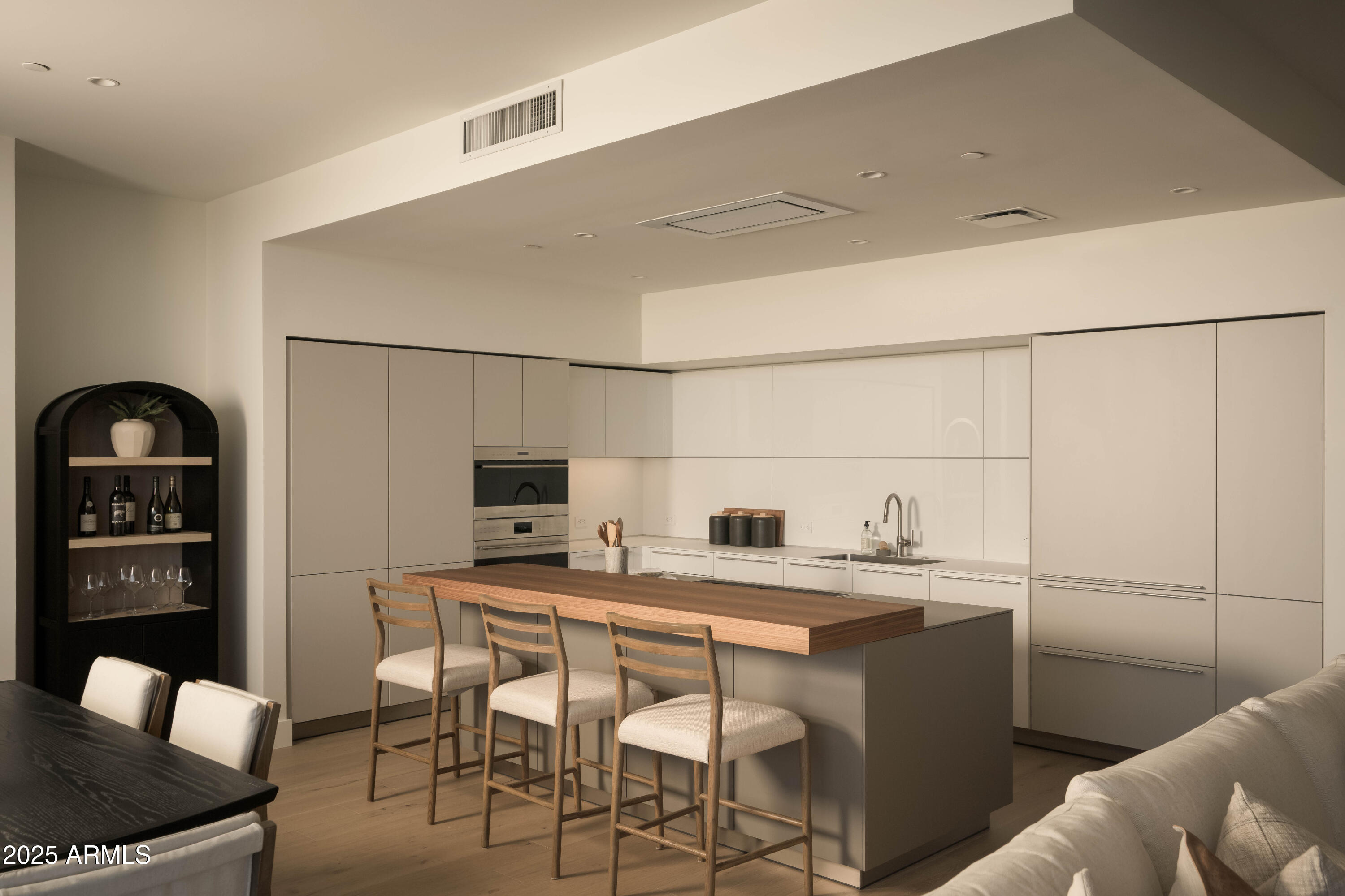 Modern kitchen with a large wood-topped island, three bar stools, and sleek built-in appliances.