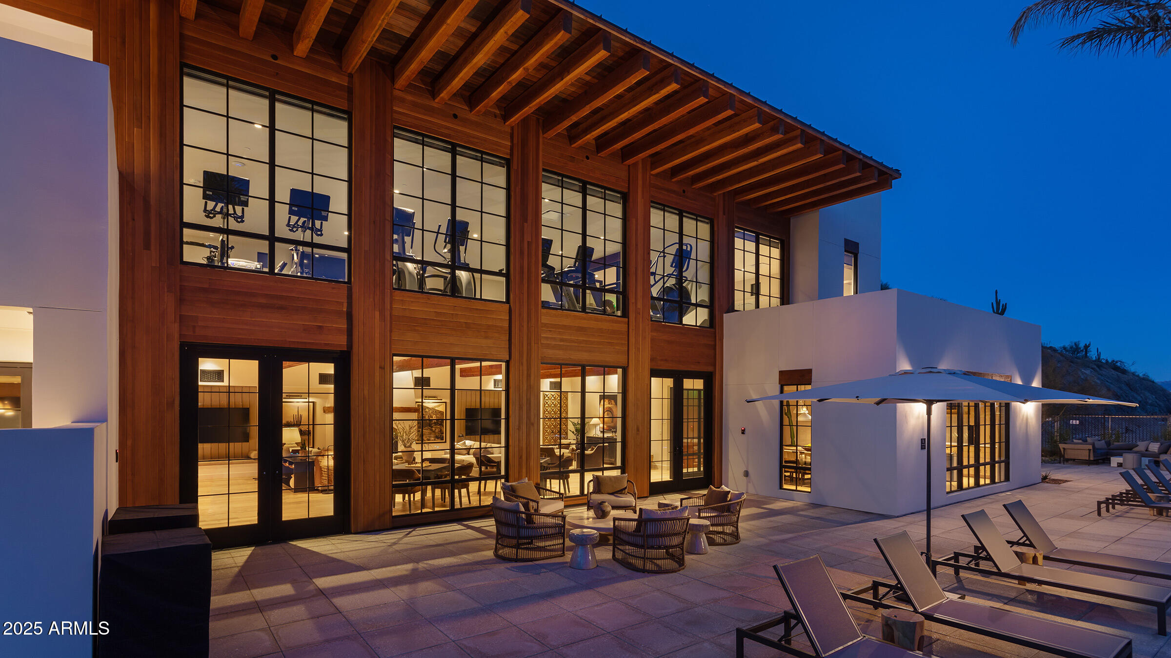 Modern home with a dramatic wood-and-glass facade and furnished patio at dusk.