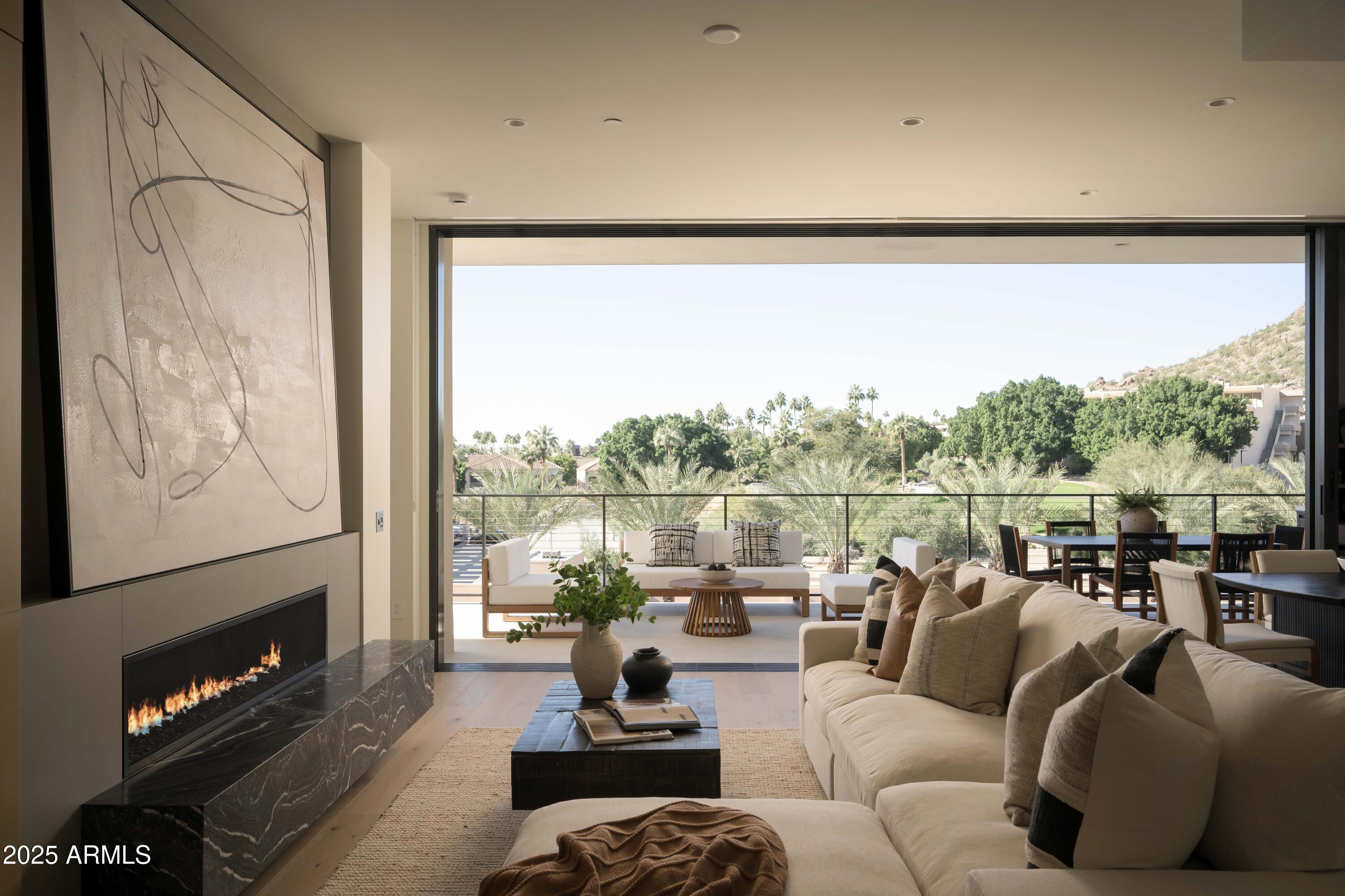 Furnished living room with a linear fireplace and open terrace overlooking palms and a desert hillside.