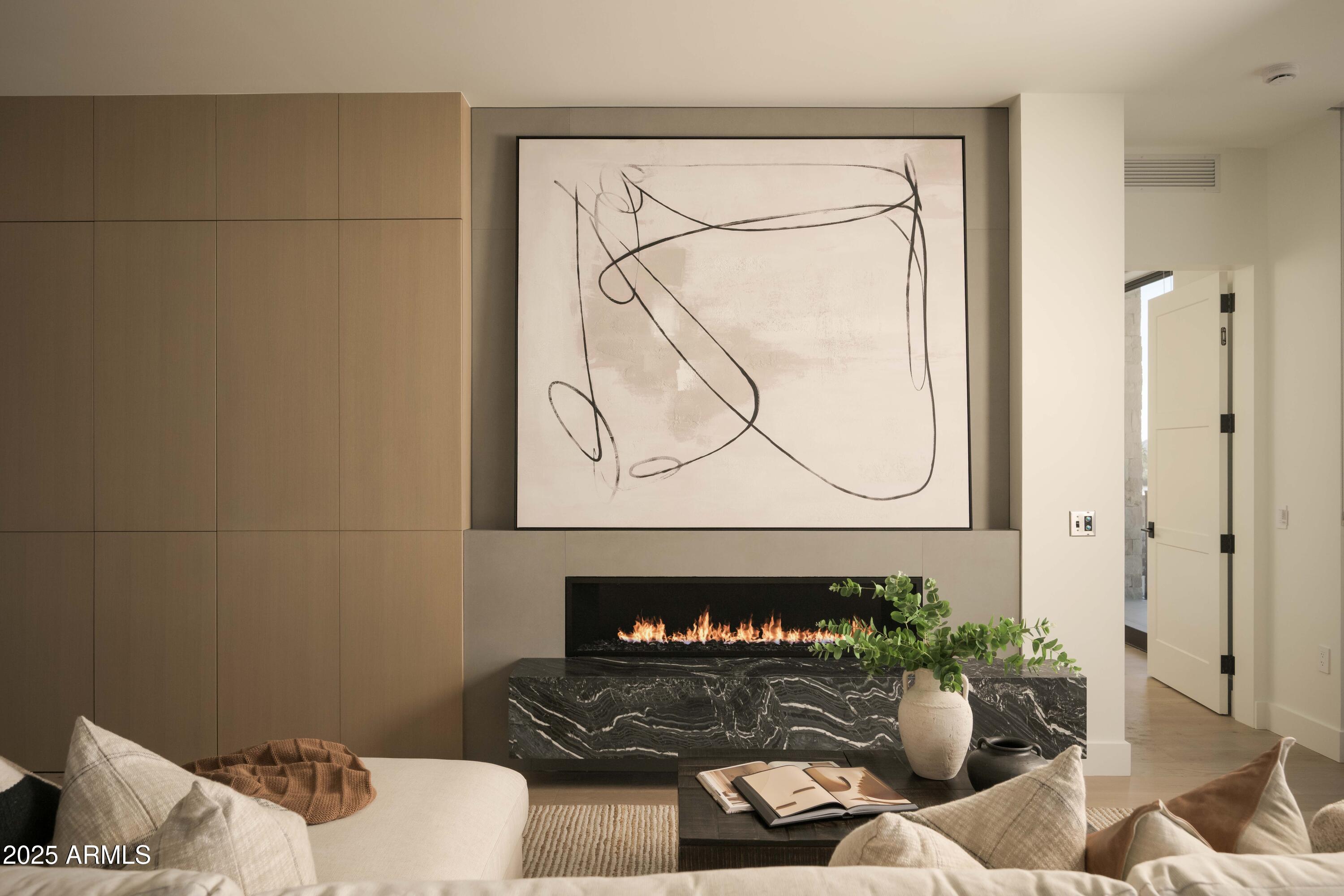 Staged living room with a linear fireplace, veined marble hearth, abstract artwork, and warm wood cabinetry.