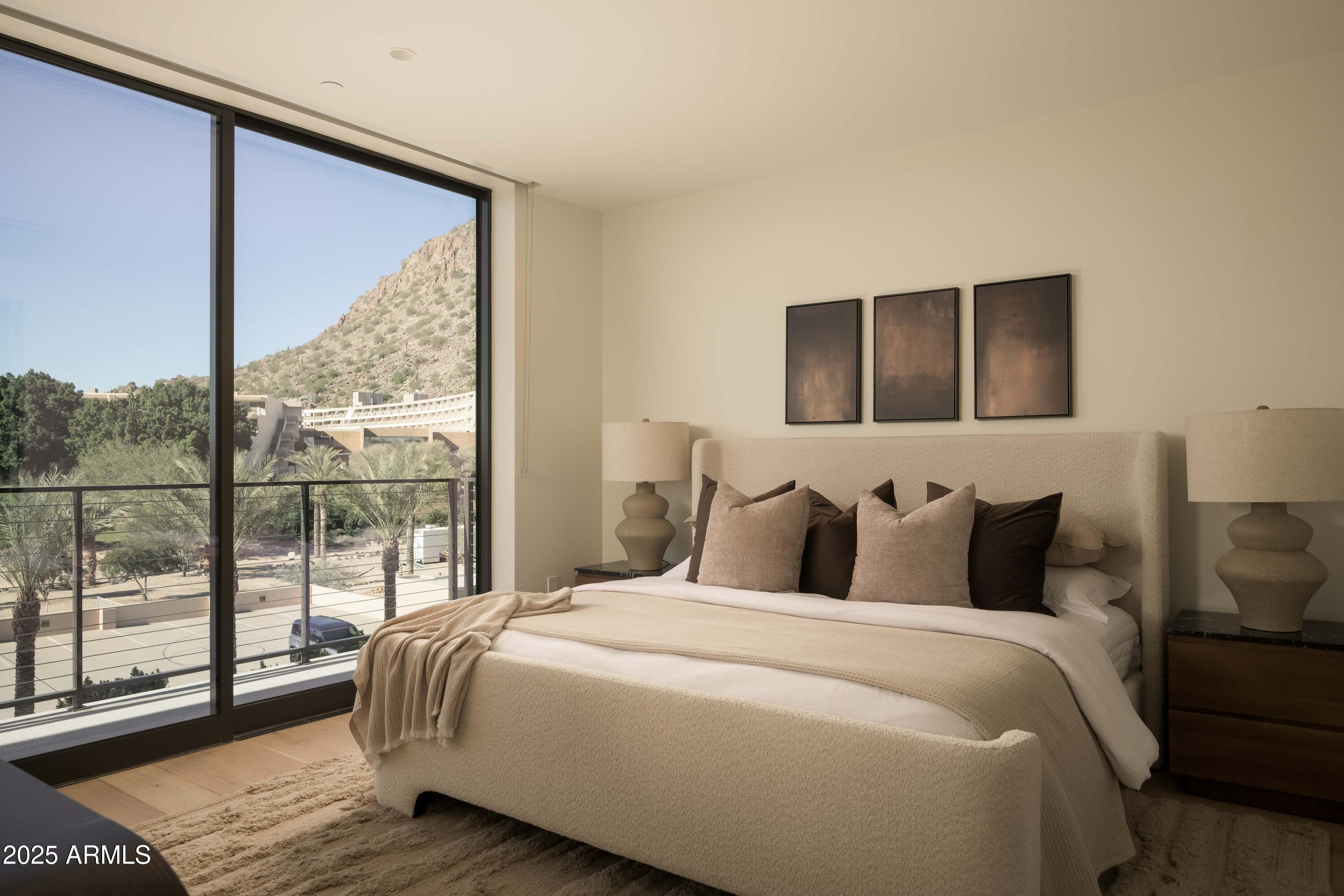 Bedroom with a neutral upholstered bed and floor-to-ceiling windows overlooking a rocky mountain slope.