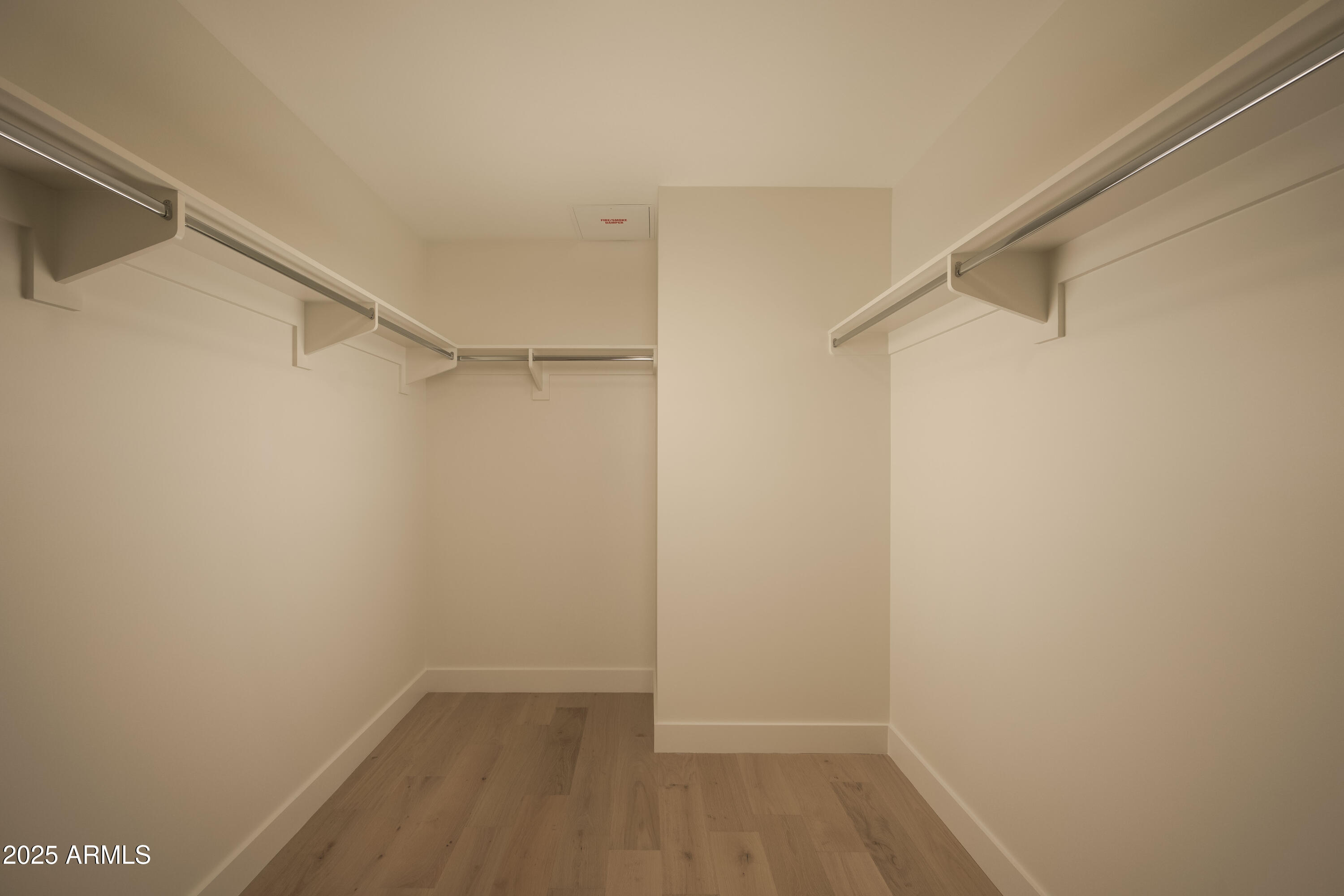 Empty walk-in closet with wood-look flooring, wraparound hanging rods, and a central partition.