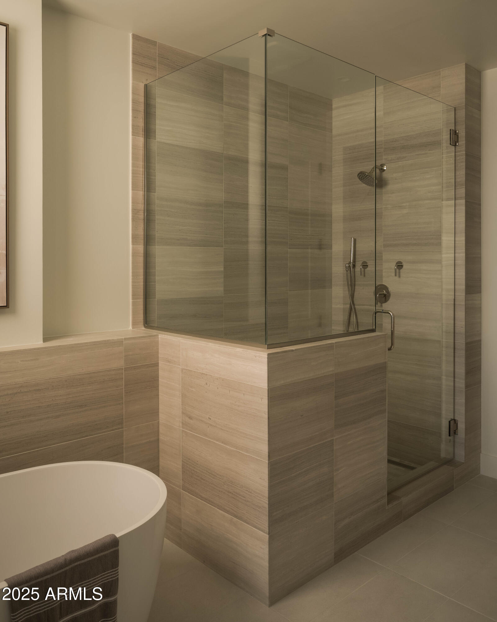 Stone-tiled walk-in shower with clear glass enclosure beside a freestanding soaking tub.