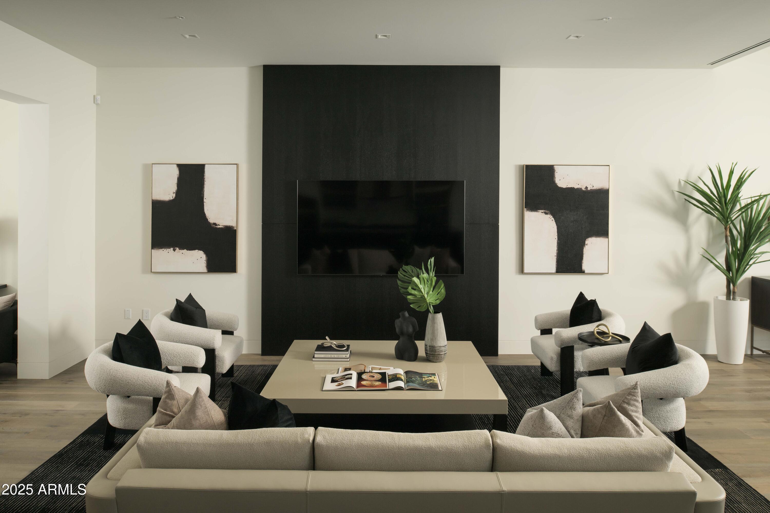 Modern living room with a black television wall, cream lounge chairs, and abstract artwork.