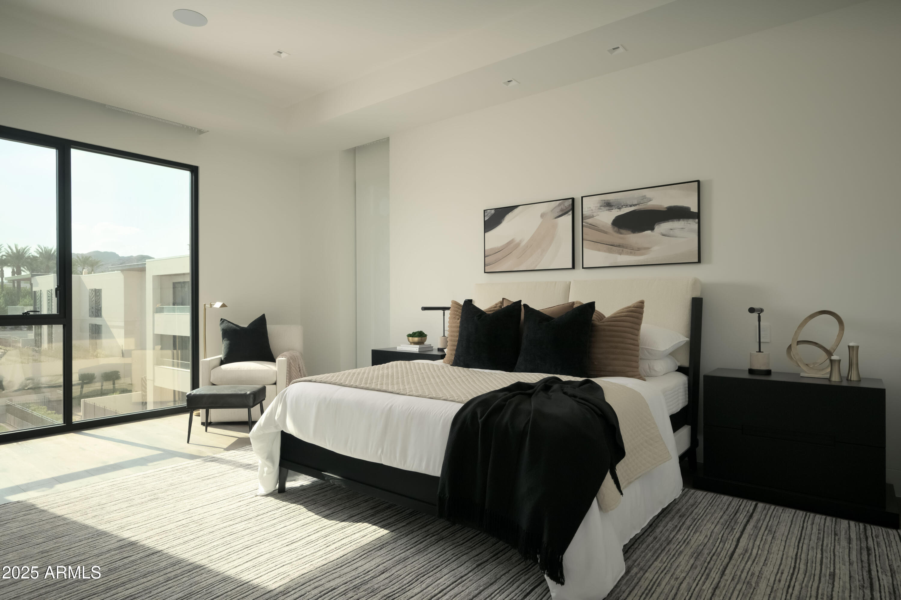 Furnished bedroom with a king bed, abstract wall art, and floor-to-ceiling windows overlooking distant mountains.