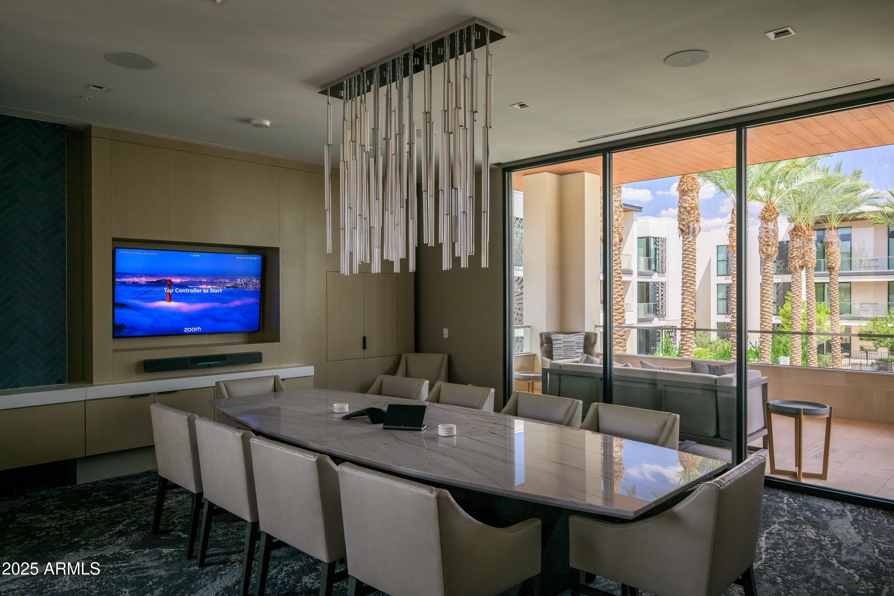 Modern dining room with a long marble table and floor-to-ceiling windows overlooking palm trees.