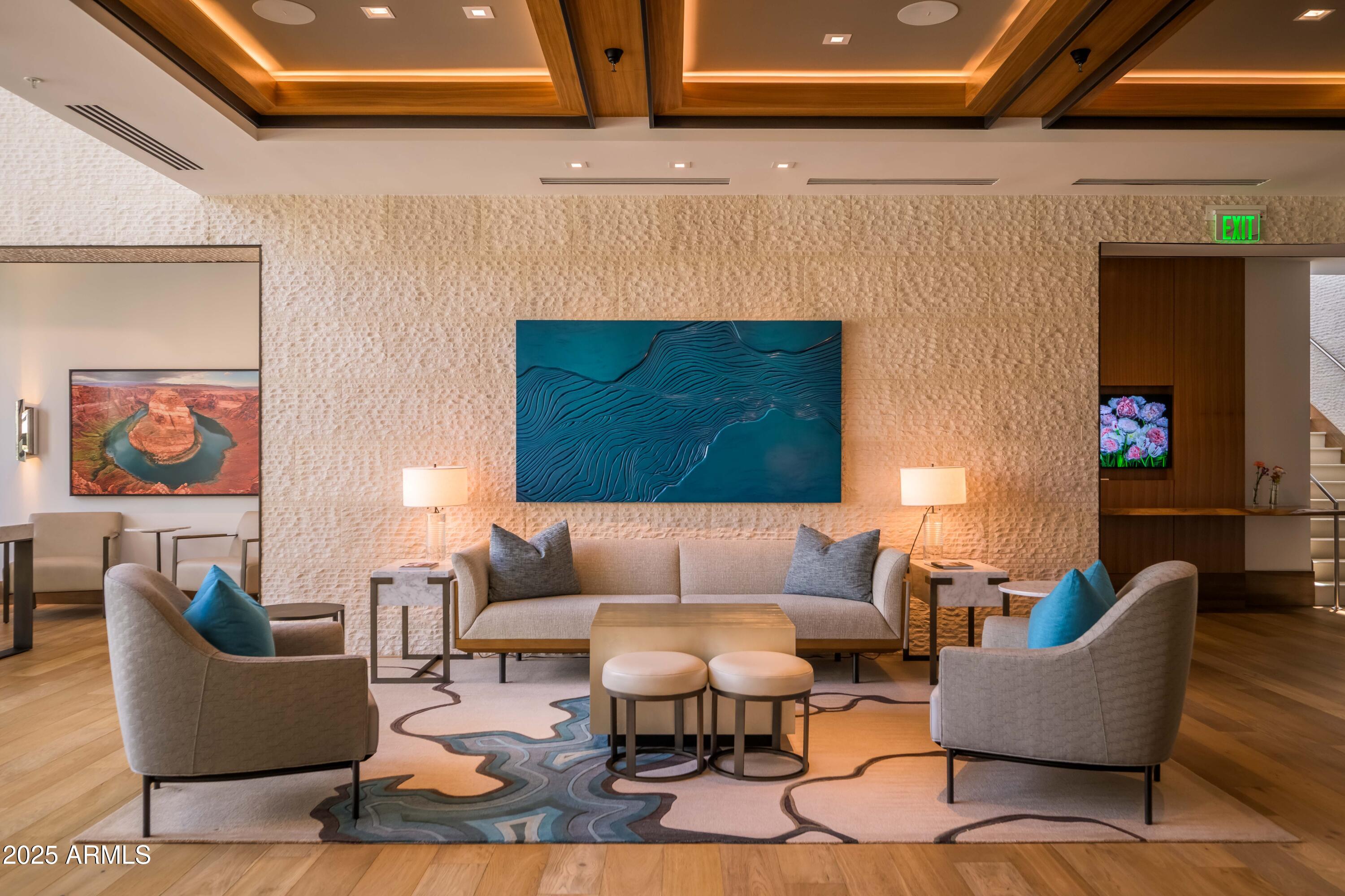 Furnished lounge with a cream sofa, gray armchairs, blue wall art, and a textured stone wall.