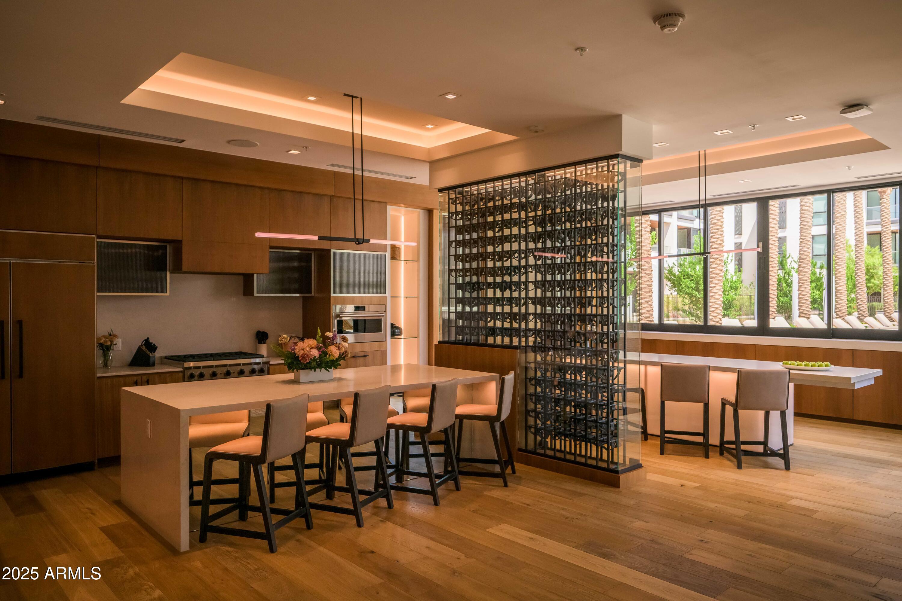 Modern kitchen with a large island, glass wine display, and windows overlooking palm trees.