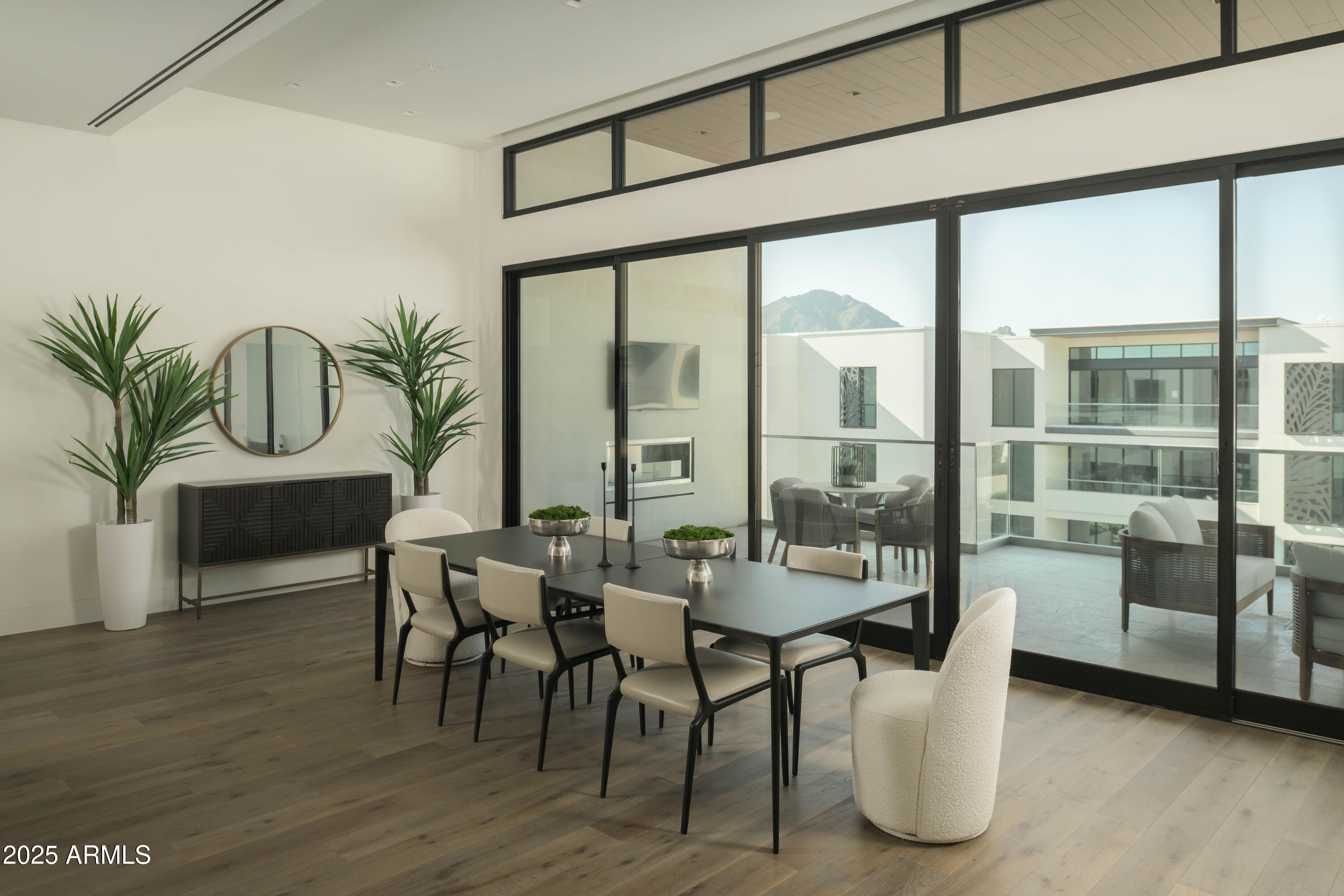 Dining room with a dark table and cream chairs beside glass doors overlooking a balcony and mountain.