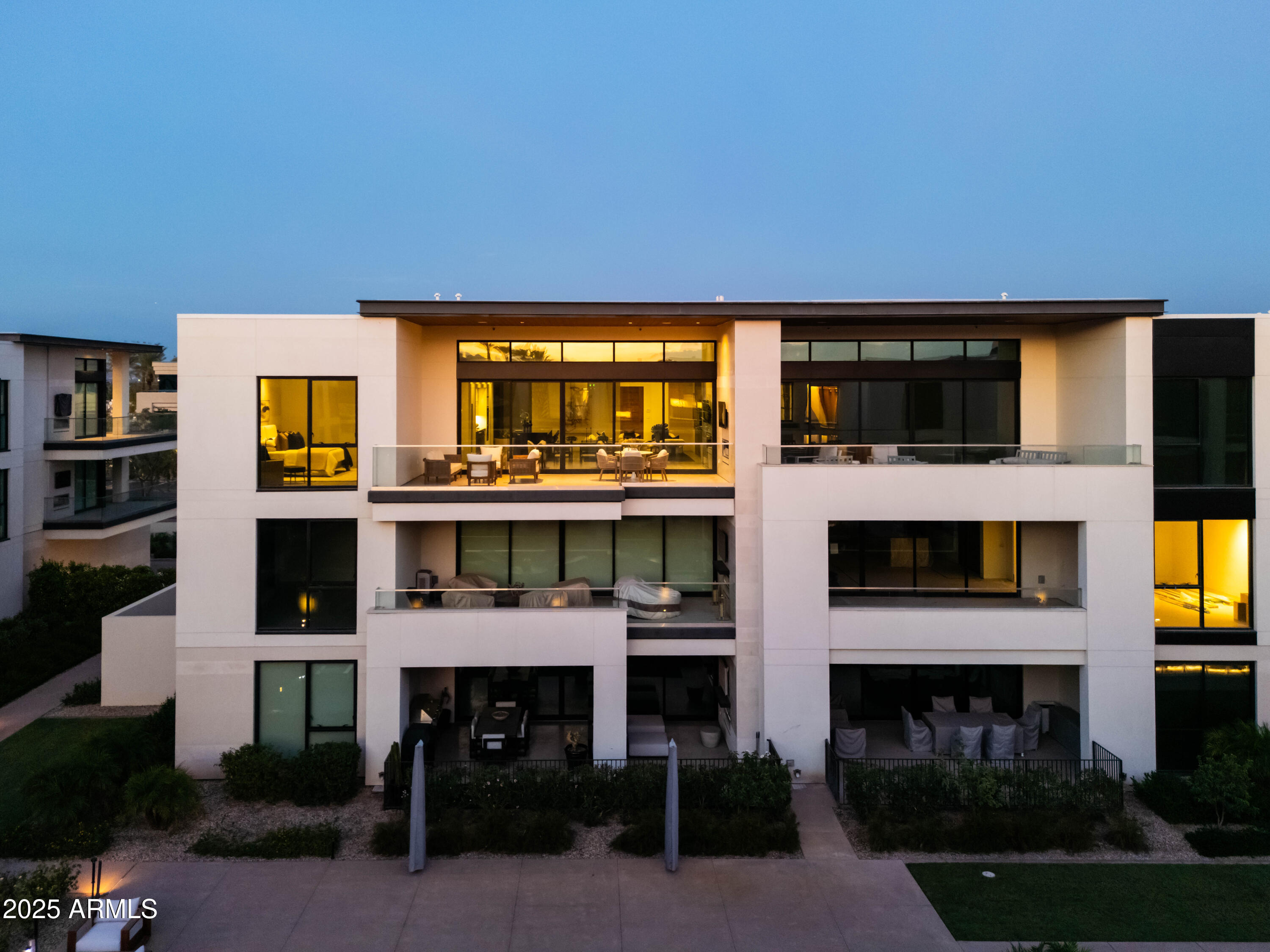 Modern multi-story residence with glass balconies and warmly lit windows at dusk.