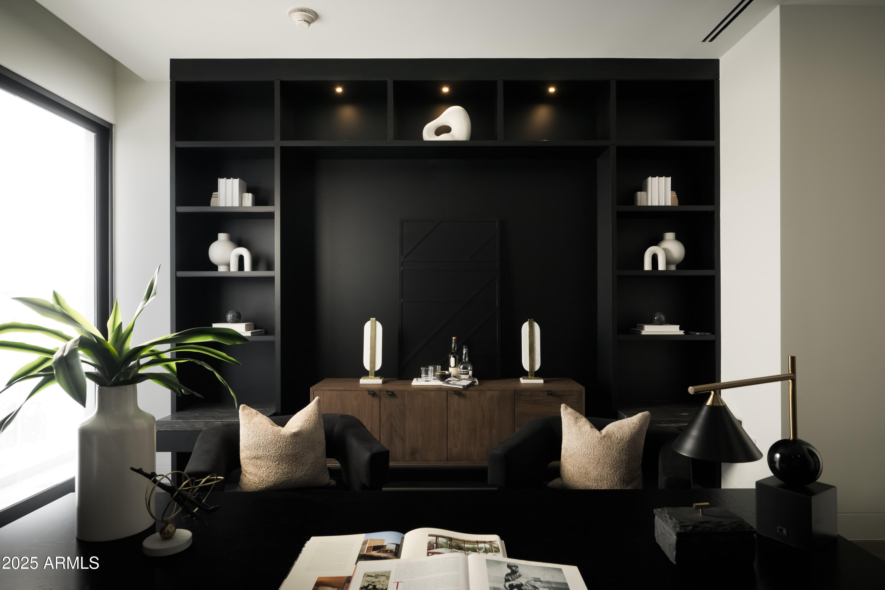 Sitting area with black built-in shelves, a wood cabinet, and two armchairs beside a large window.