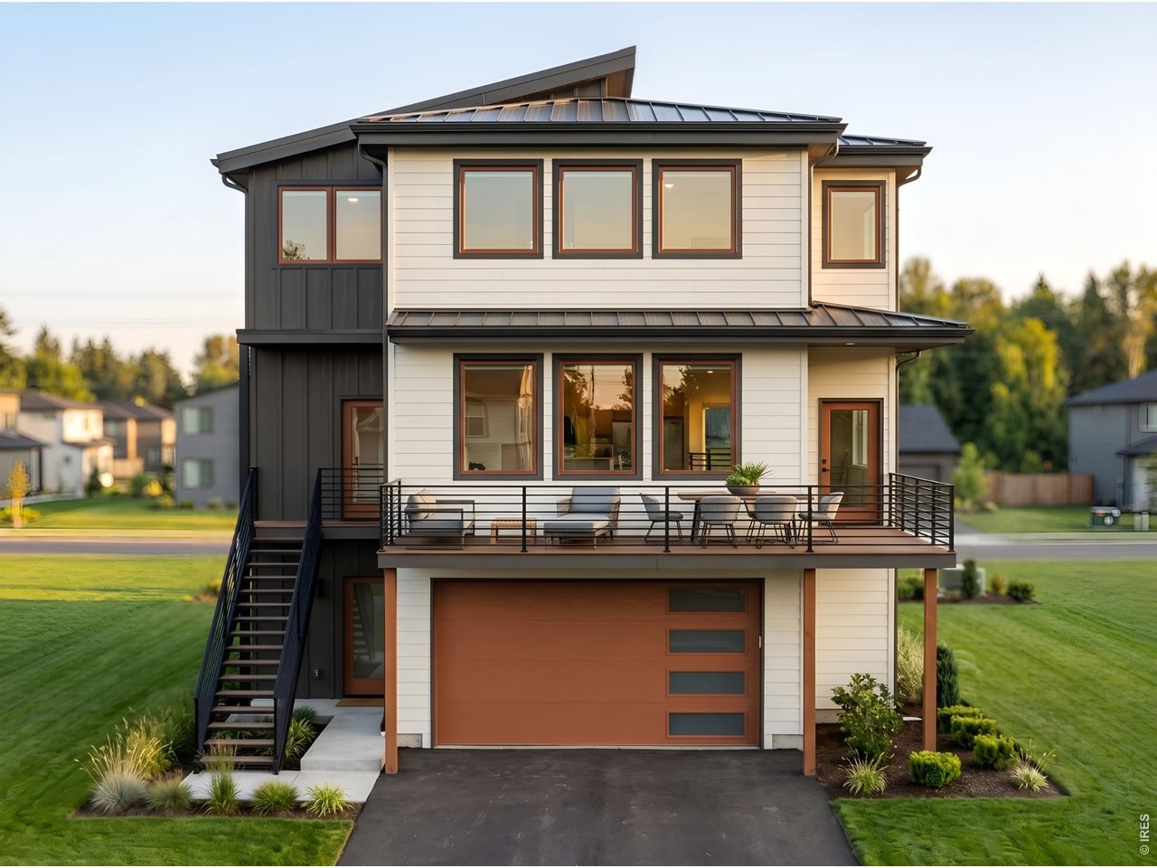 Modern two-story home with a furnished balcony, exterior staircase, and orange-brown garage door.