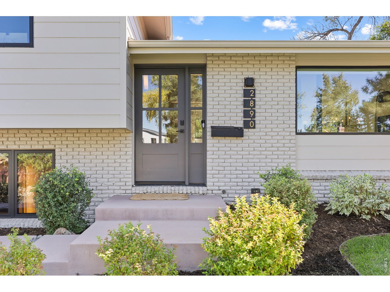 Modern home entrance with white brick, gray door, landscaped shrubs, and house number 2890.