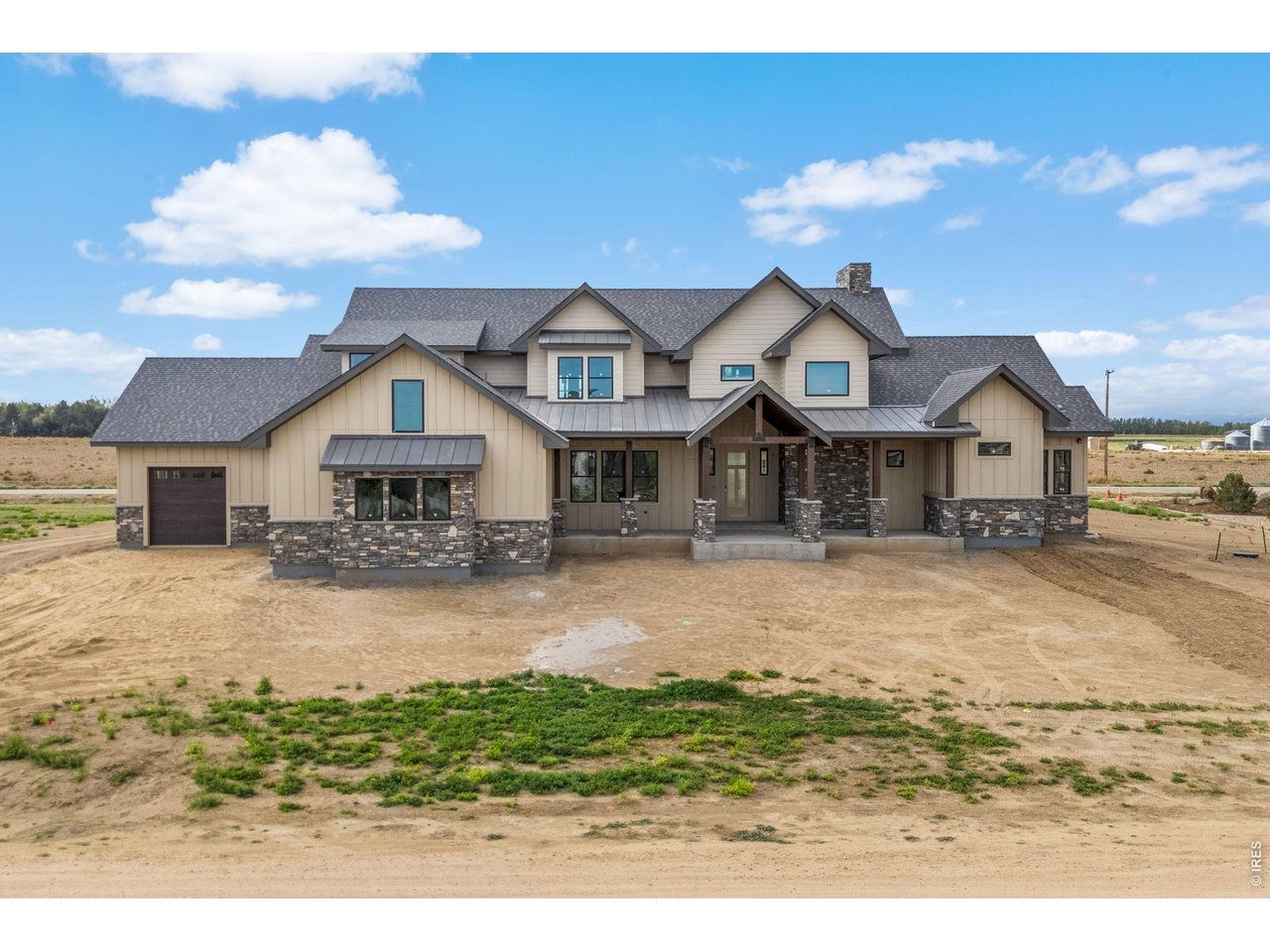 Large beige house with stone accents and an attached garage on a mostly bare lot.