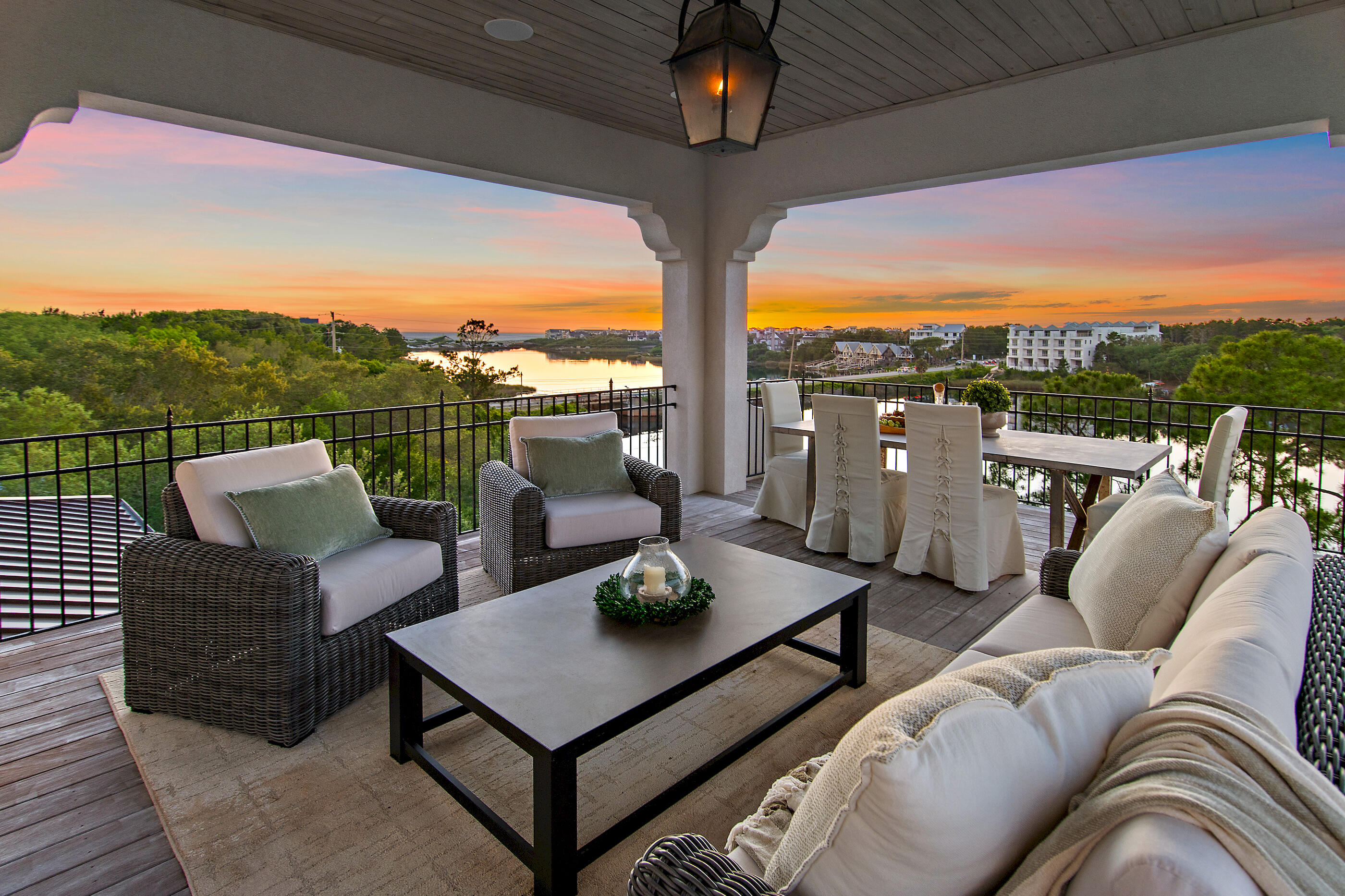Covered terrace with wicker seating and dining area overlooking a waterway at sunset.