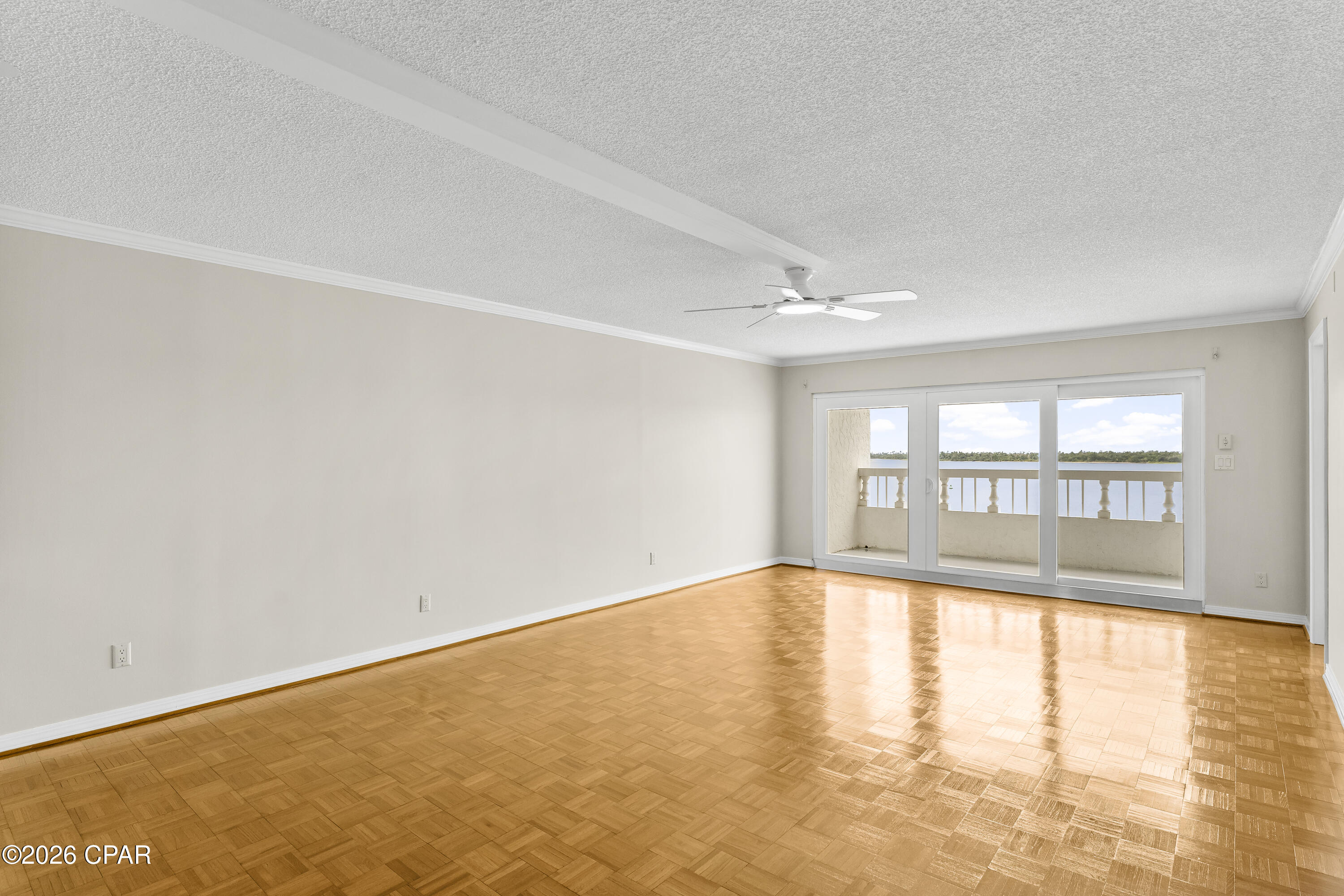 Empty living room with parquet floors and sliding doors overlooking water.