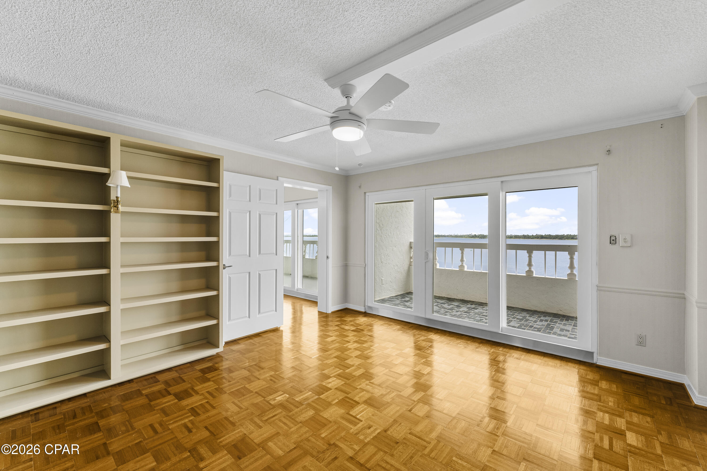 Vacant room with built-in shelves, parquet flooring, and balcony doors overlooking the water.