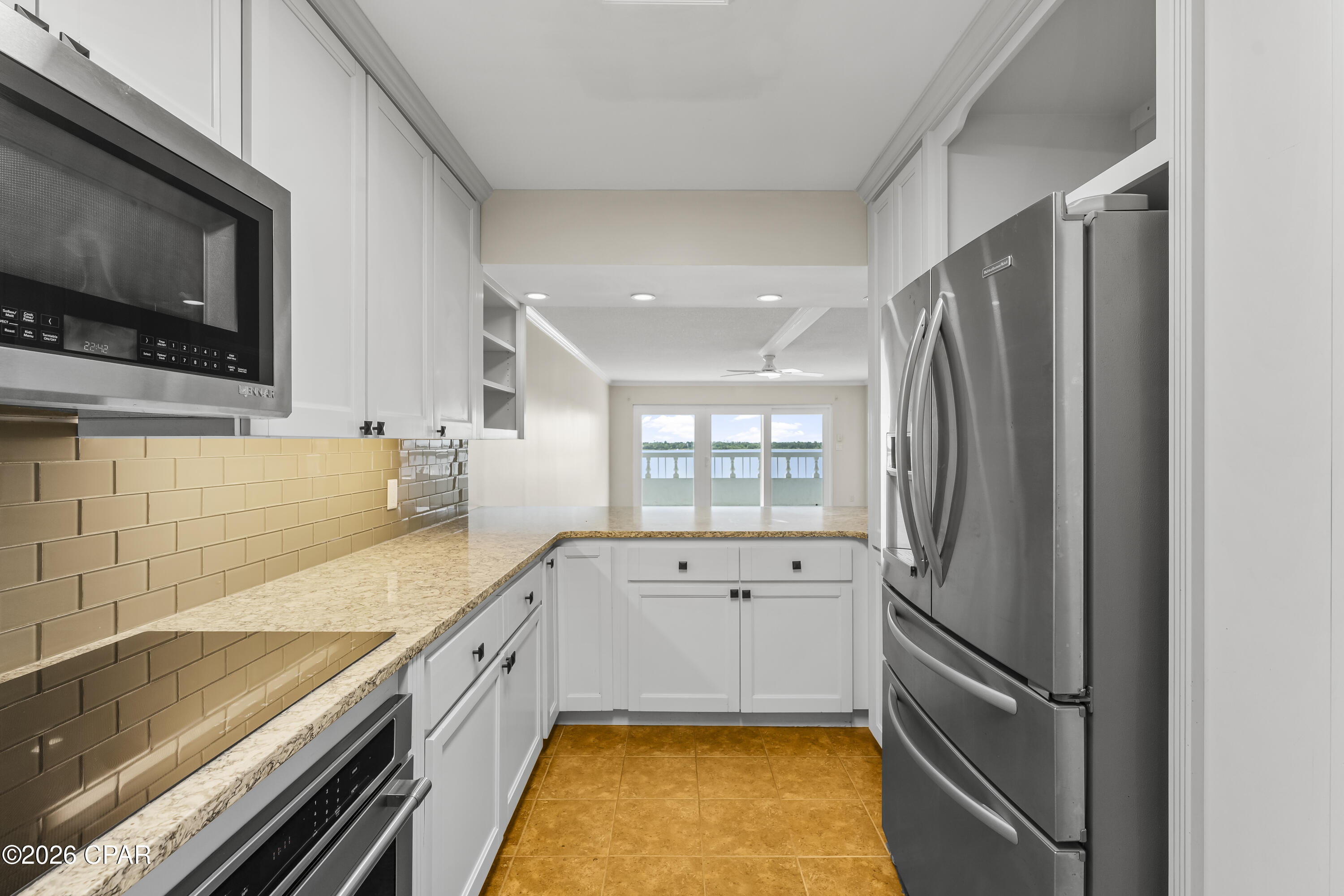 Kitchen with white cabinets and stainless appliances, looking through to a balcony and water view.