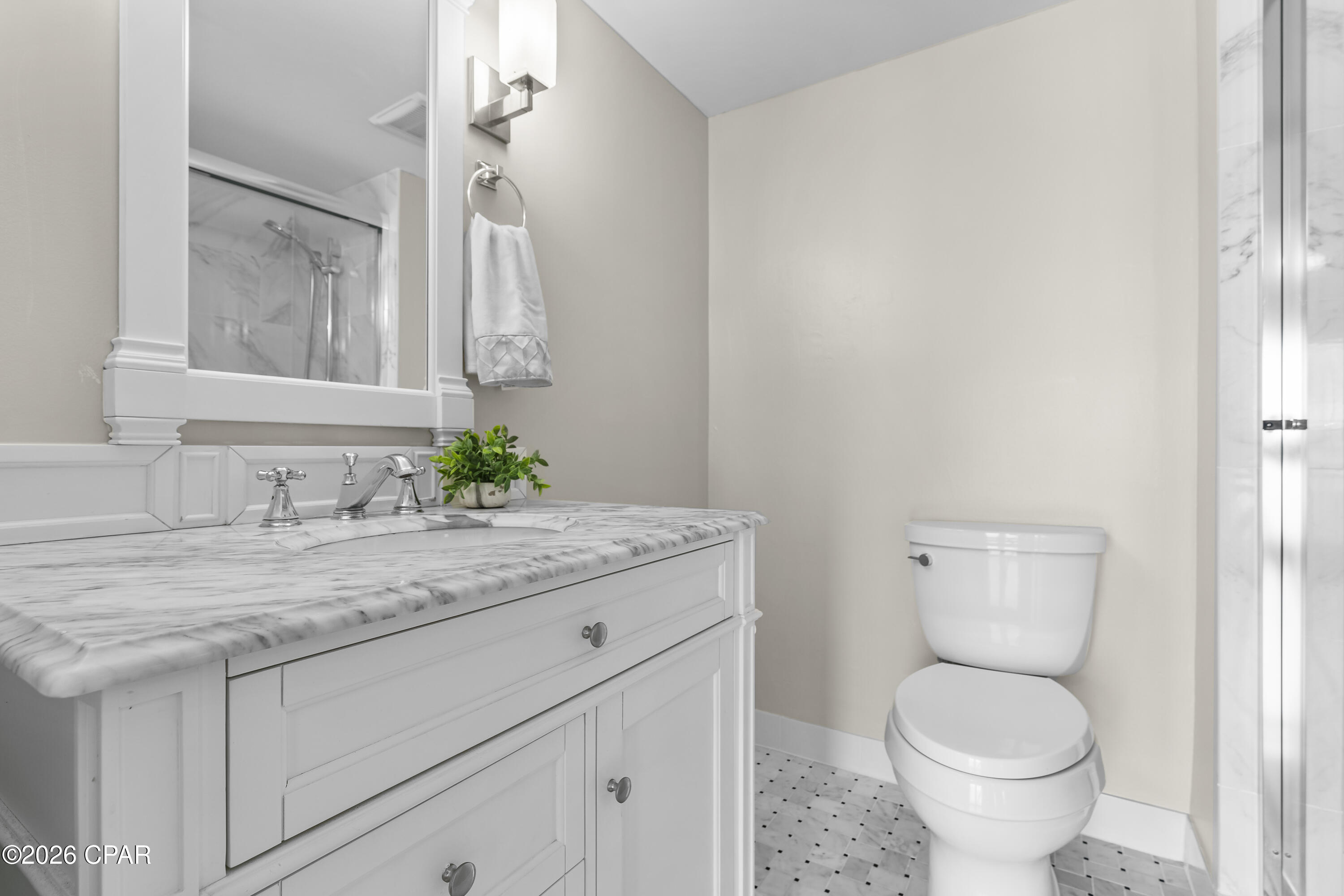 Bathroom with a marble-topped white vanity, framed mirror, and tiled shower surround.