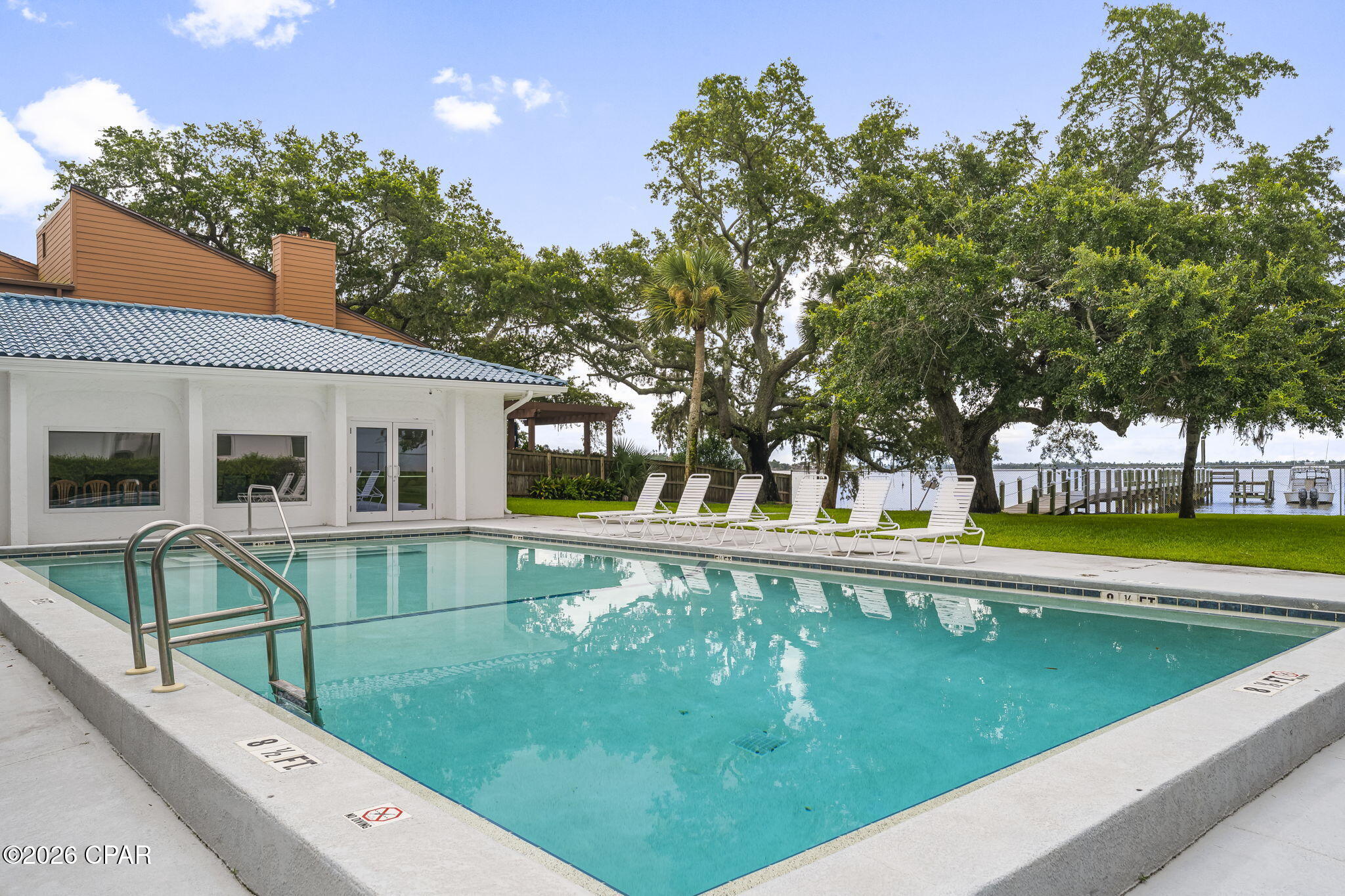 Outdoor swimming pool beside a waterfront dock, with lounge chairs and a poolside building.