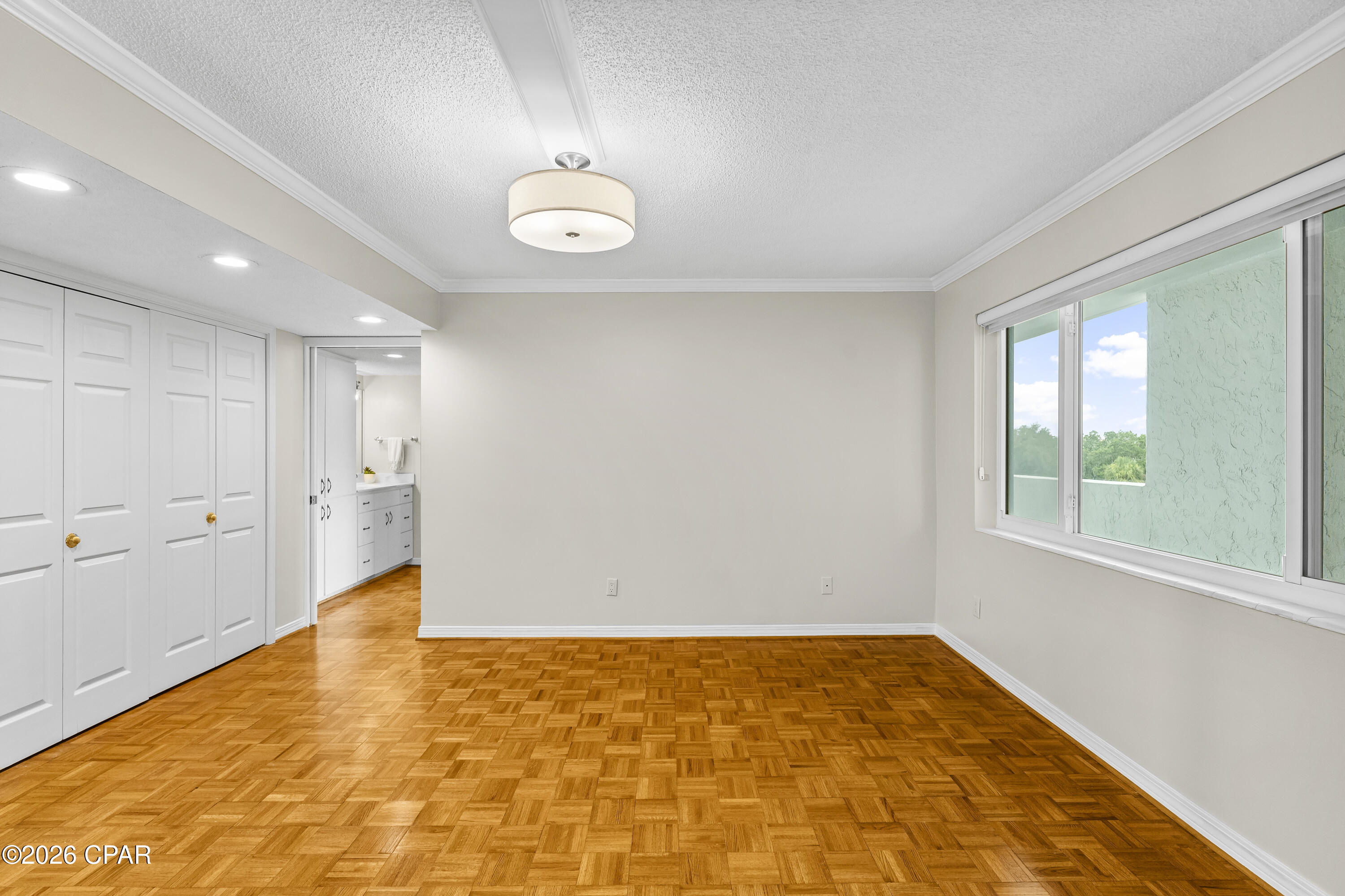 Vacant bedroom with parquet flooring, wall of closets, and a large window.