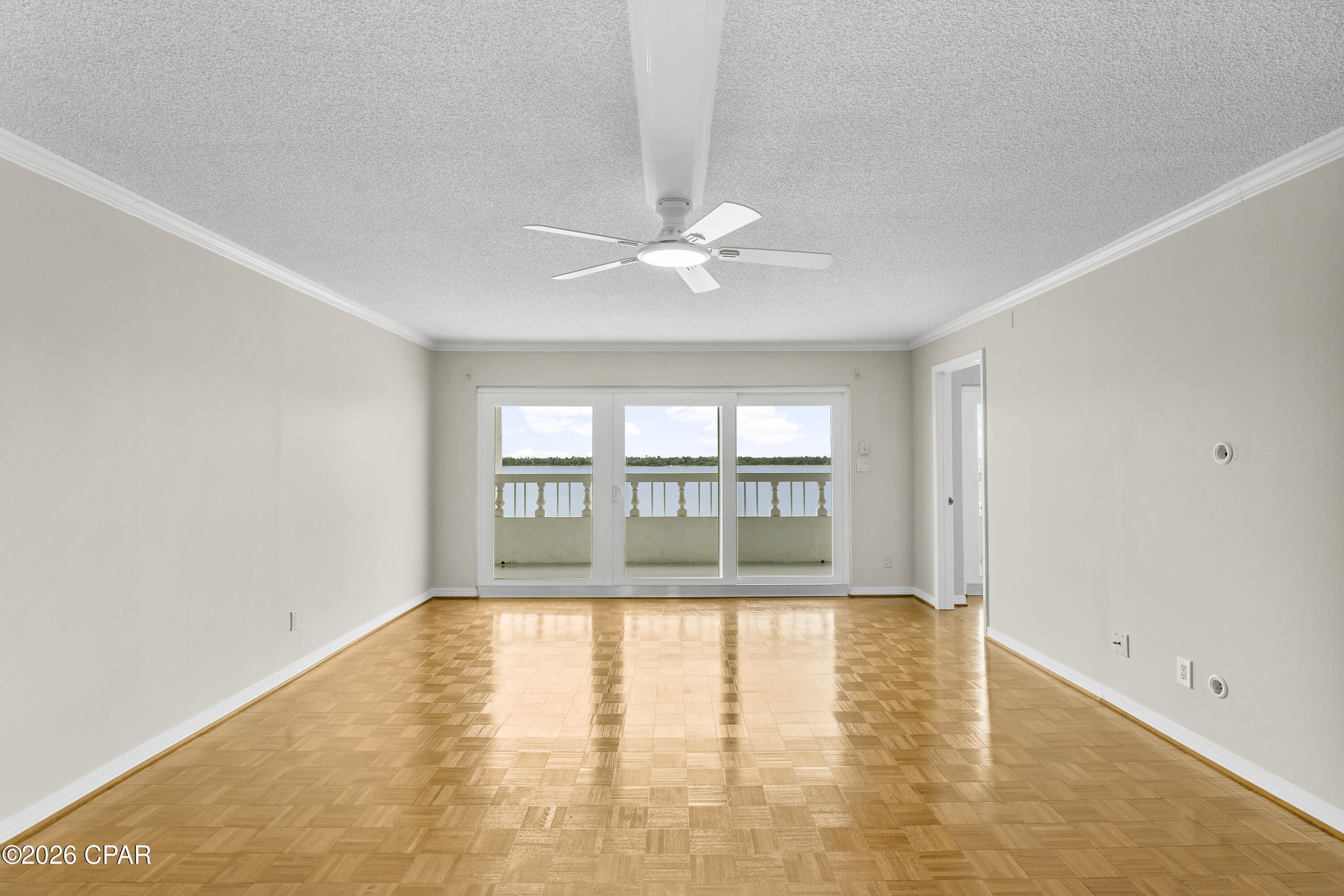 Vacant living room with parquet floors, ceiling fan, and sliding doors overlooking the water.