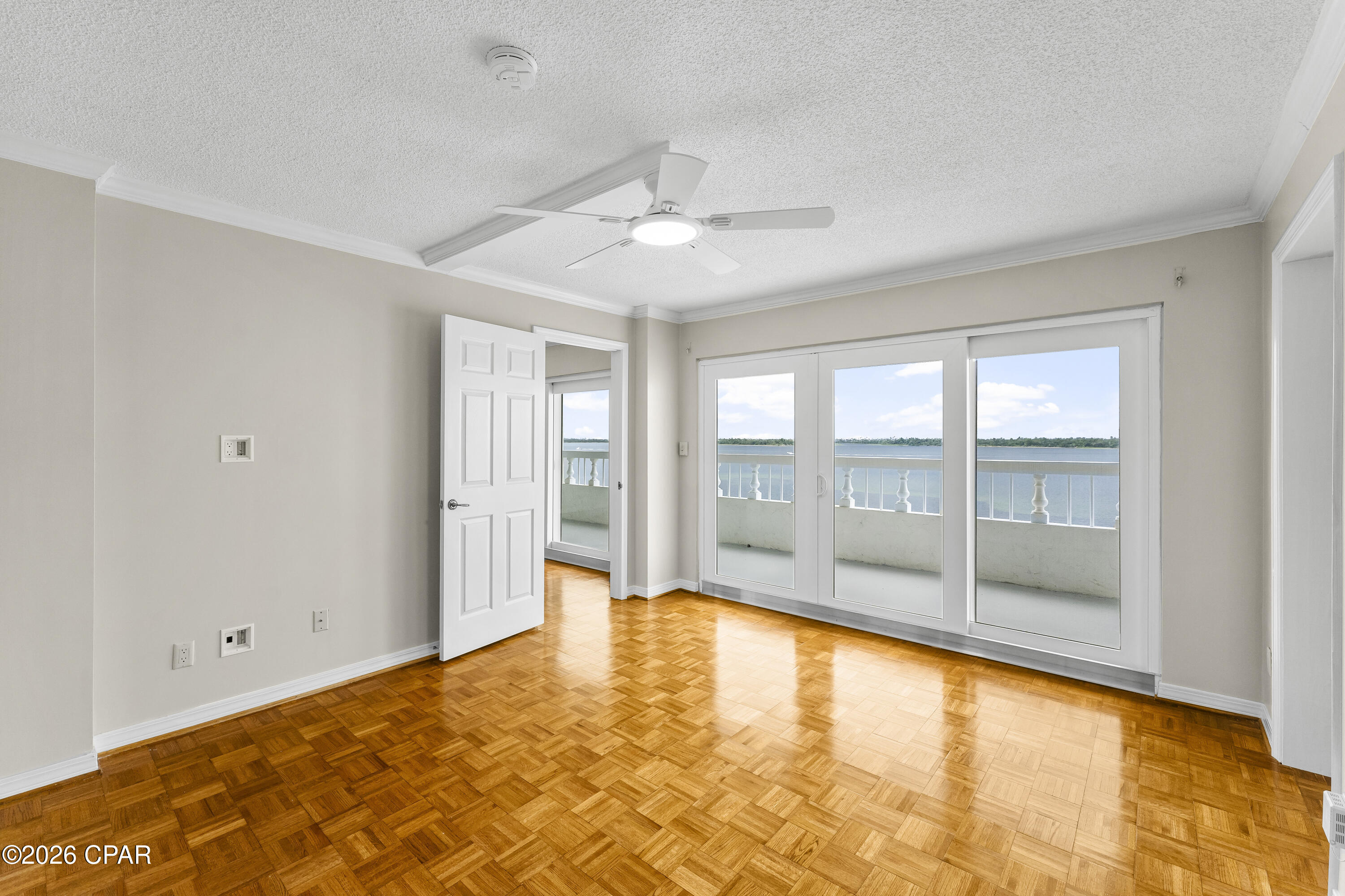 Vacant room with parquet flooring and sliding glass doors overlooking a balcony and water.