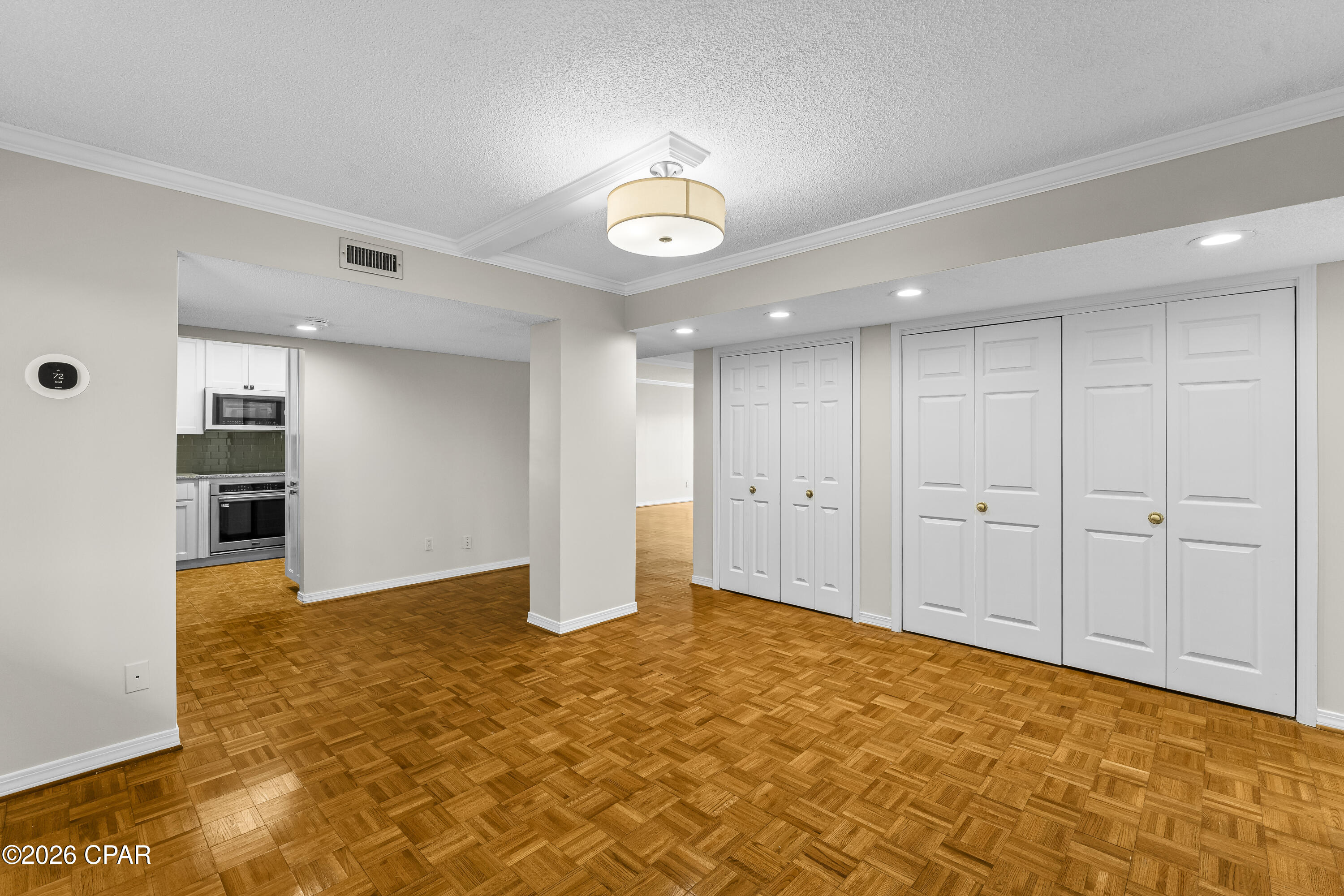 Vacant condo living area with parquet floors, white closet doors, and the kitchen visible through an open doorway.