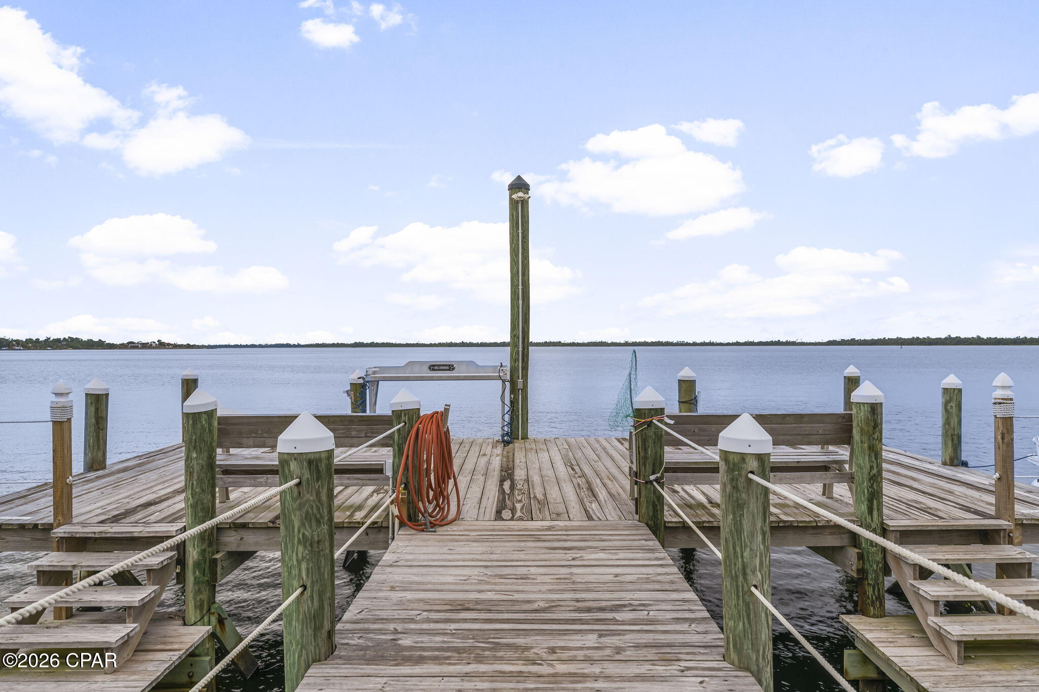 Wooden dock with mooring posts and boat lift extending into calm water.