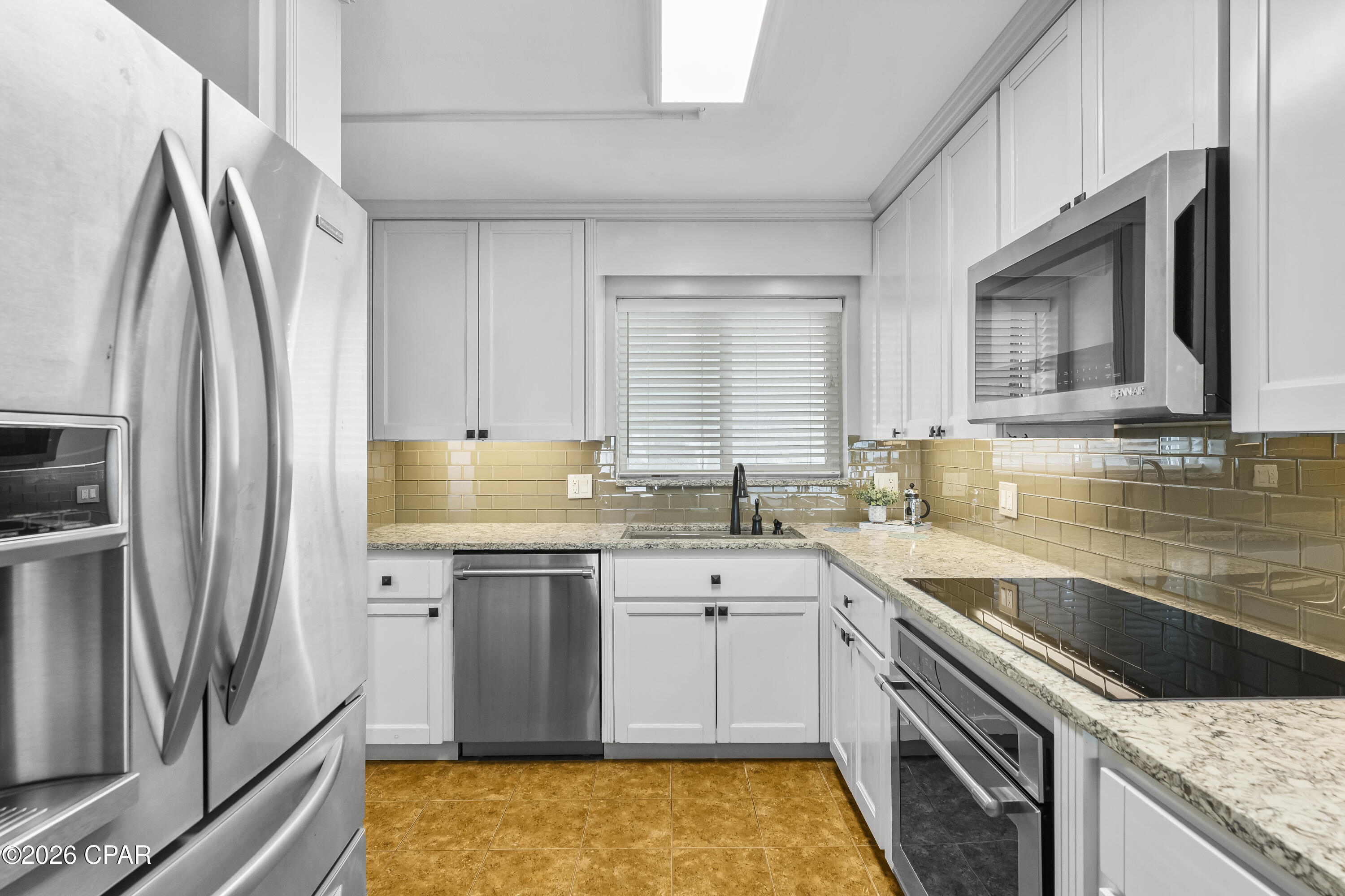 Kitchen with white cabinets, stainless appliances, gold-toned tile backsplash, and granite countertops.
