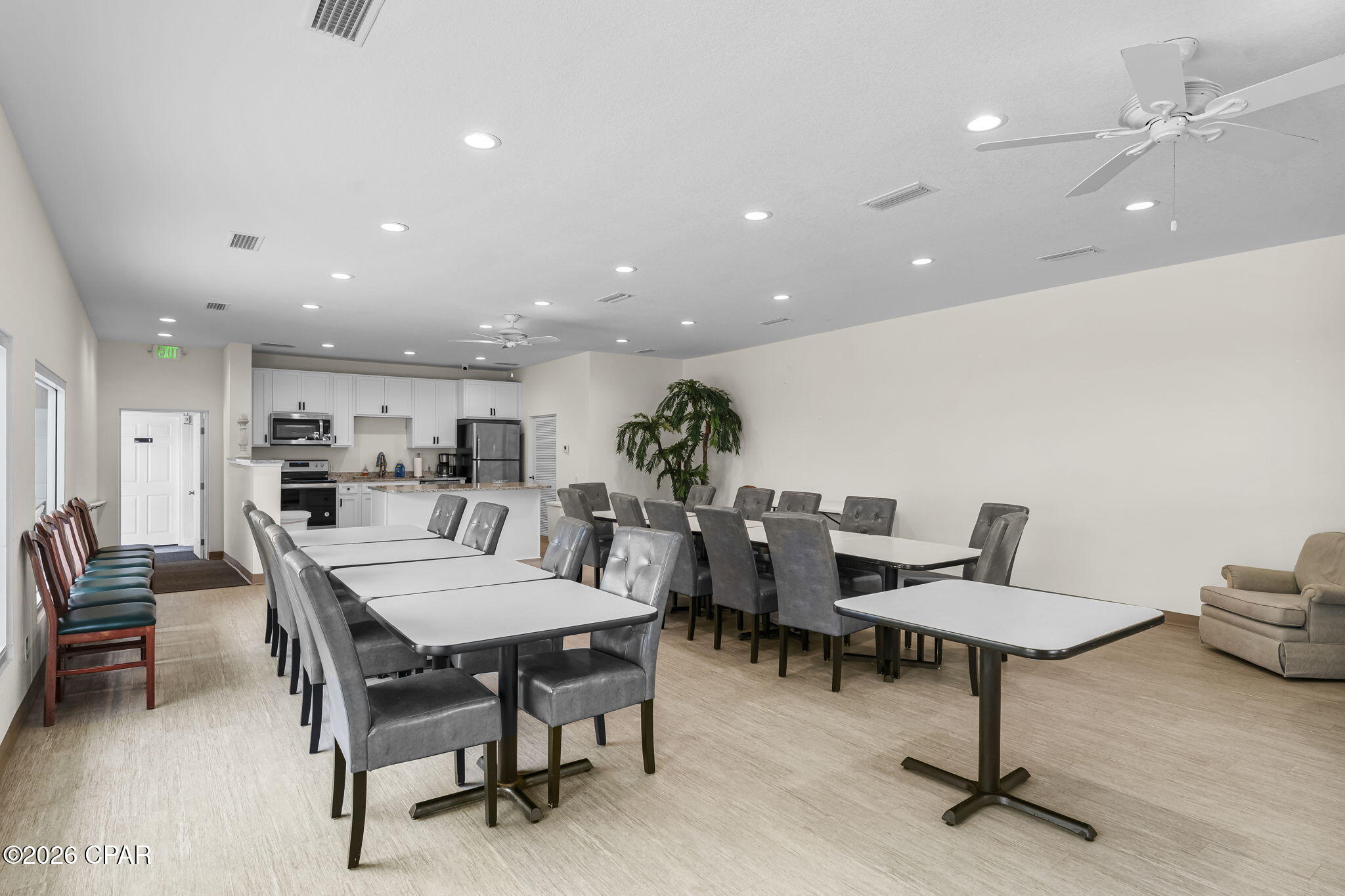 Communal meeting room with dining tables, gray chairs, and a kitchenette.