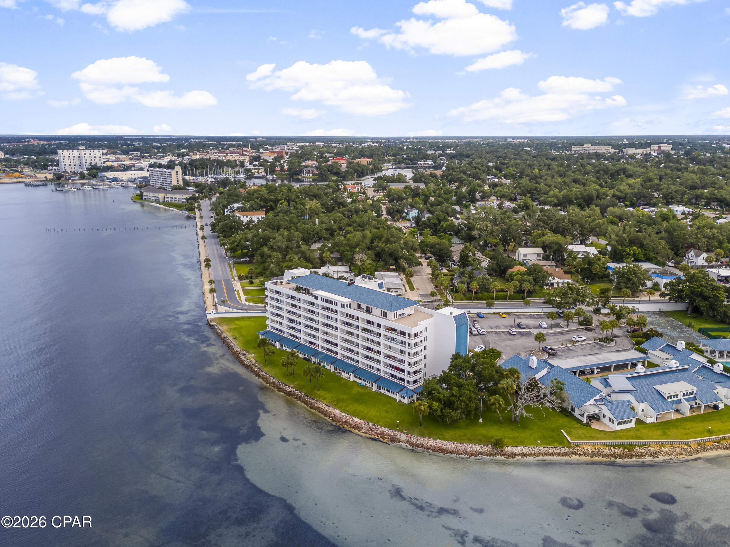 Waterfront condominium with rows of balconies beside a broad bay and tree-lined neighborhood.