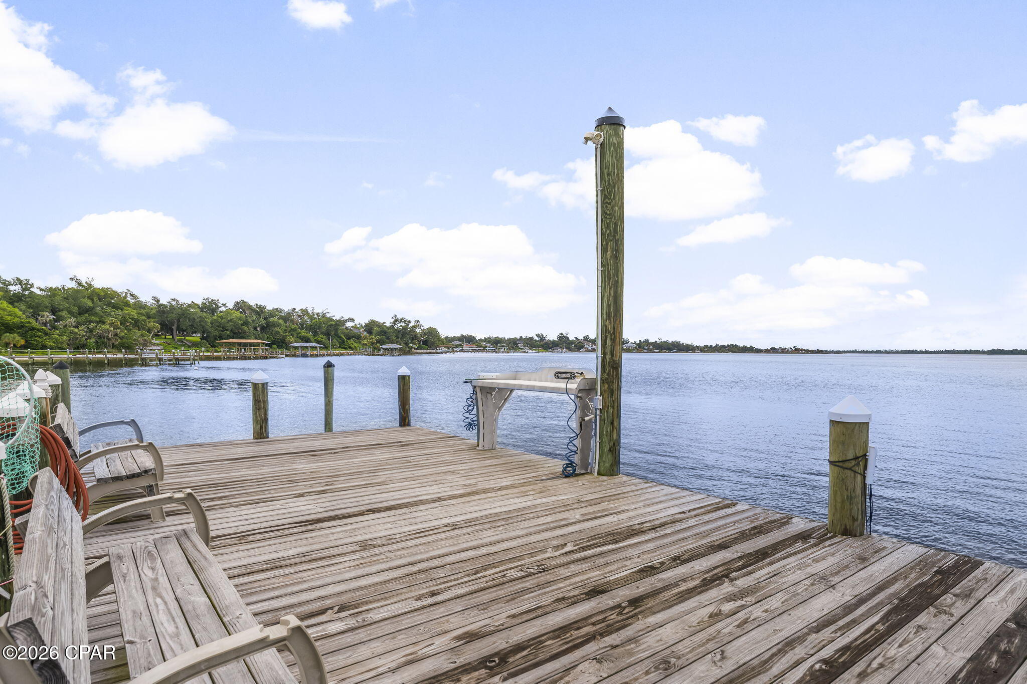 Wooden waterfront dock with a boat lift and chairs overlooking calm water.