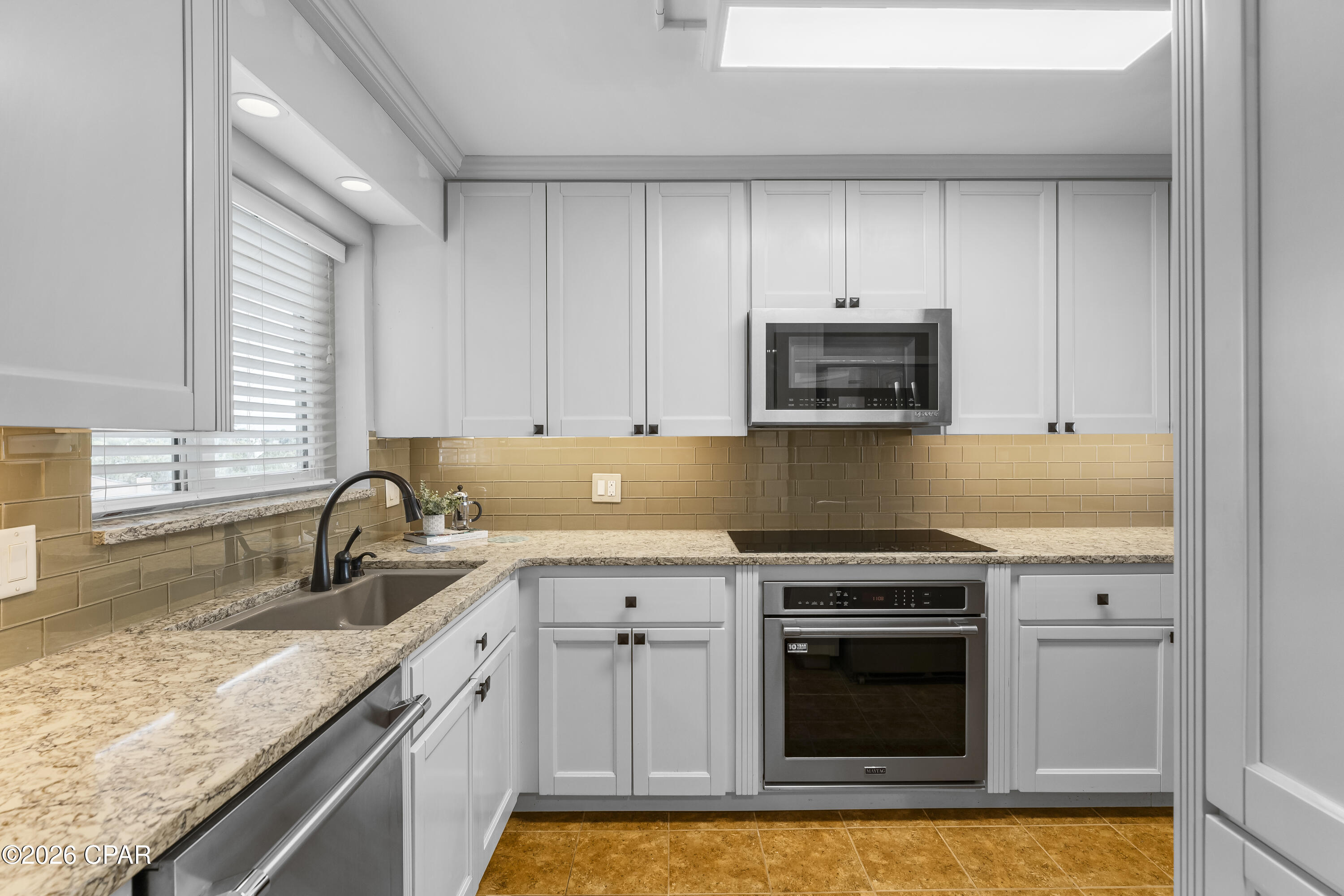 Kitchen with white cabinets, granite counters, tan tile backsplash, and stainless steel appliances.