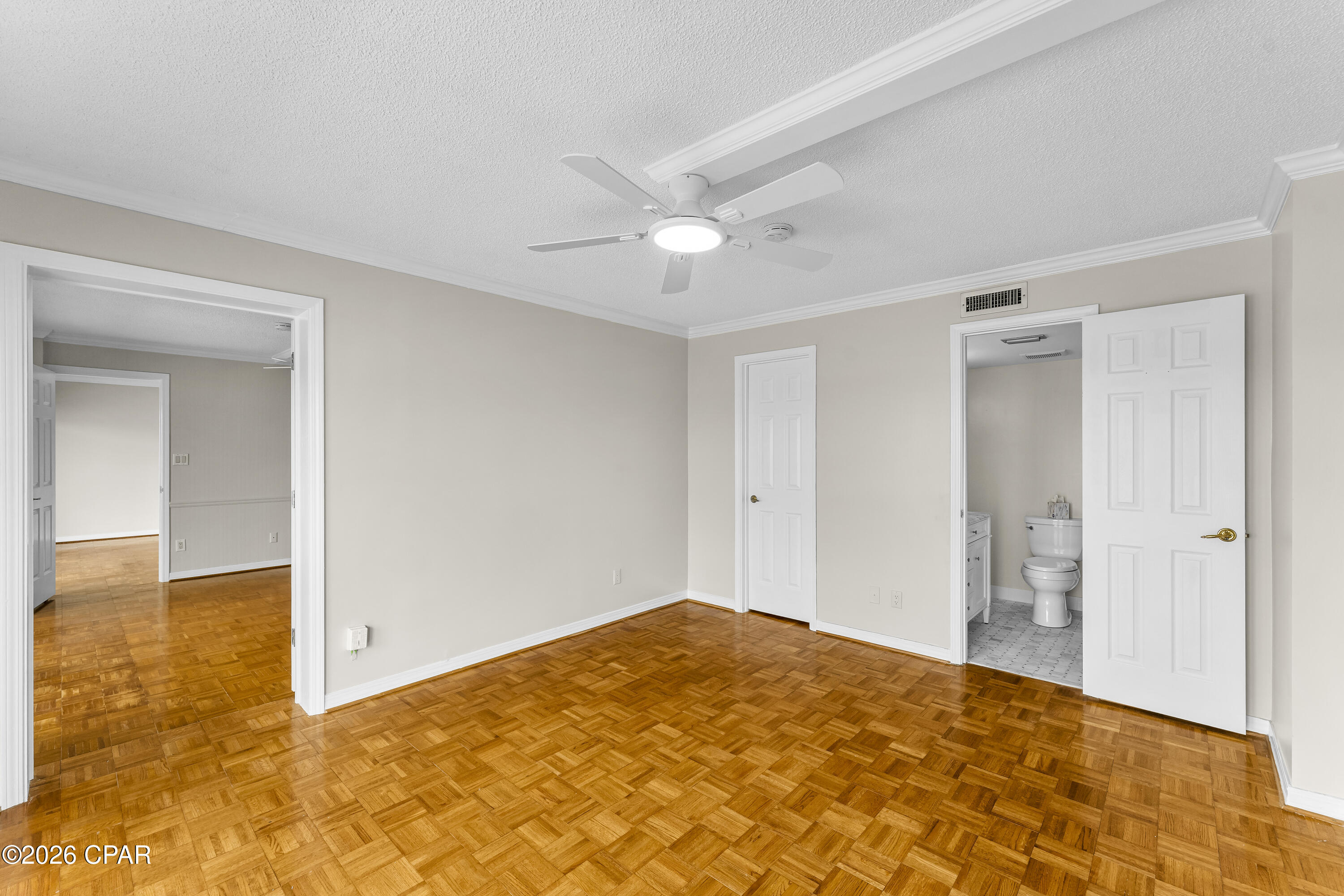 Vacant bedroom with parquet floors and ceiling fan, opening to an en suite bathroom.