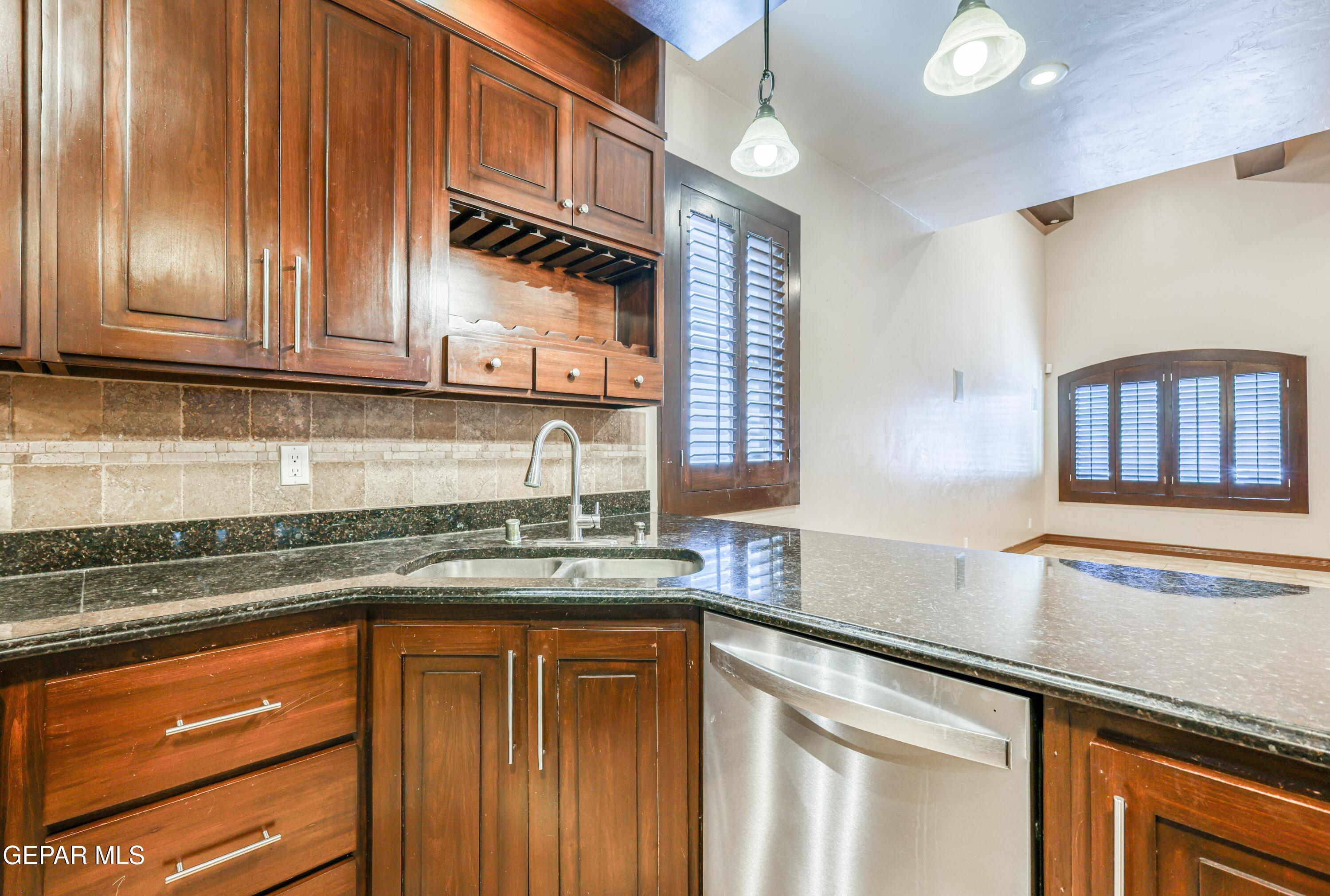 Kitchen with wood cabinets, granite counters, stainless steel dishwasher, and shuttered windows.