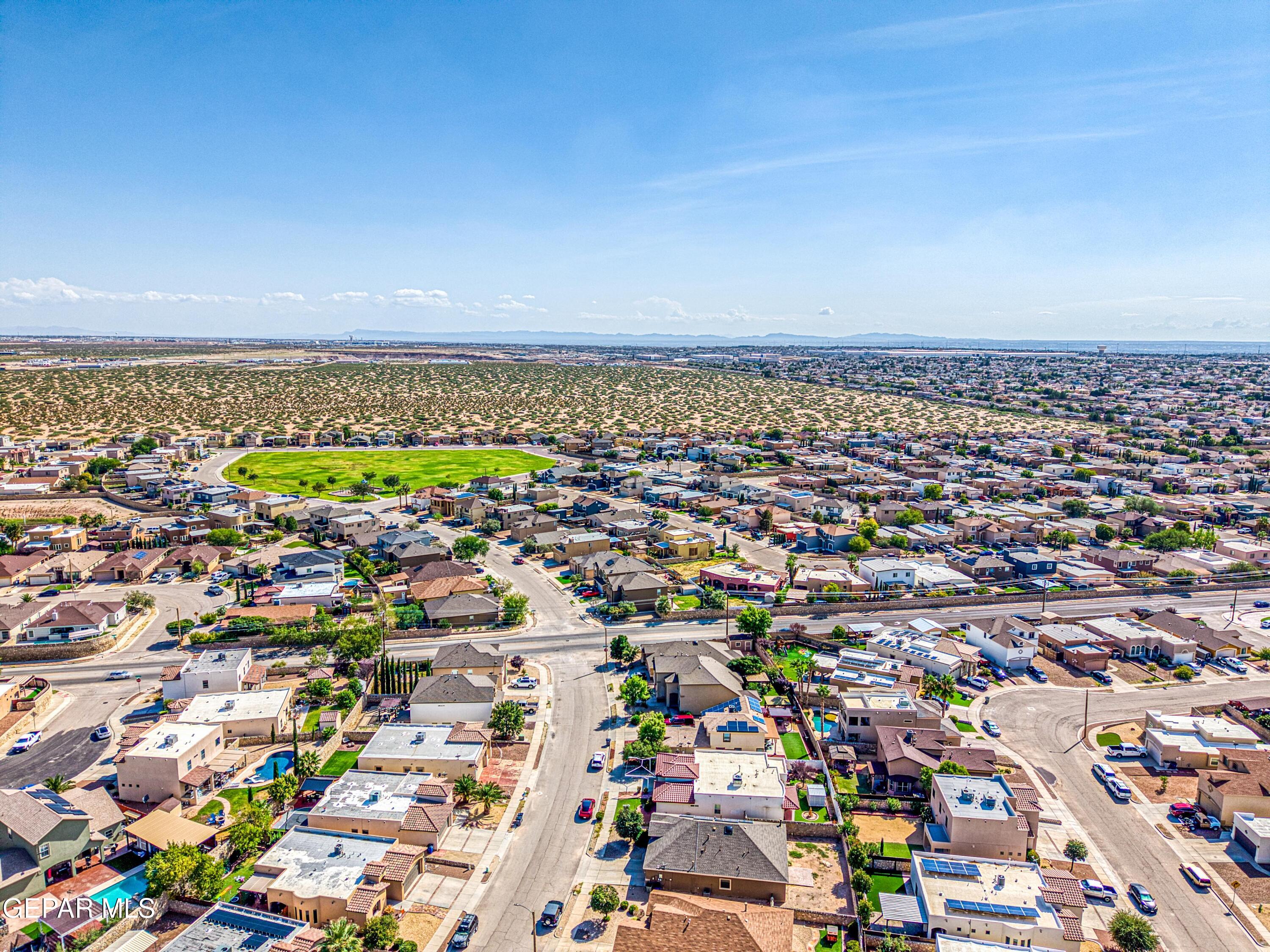 Aerial view of a suburban neighborhood with a green park and desert beyond.