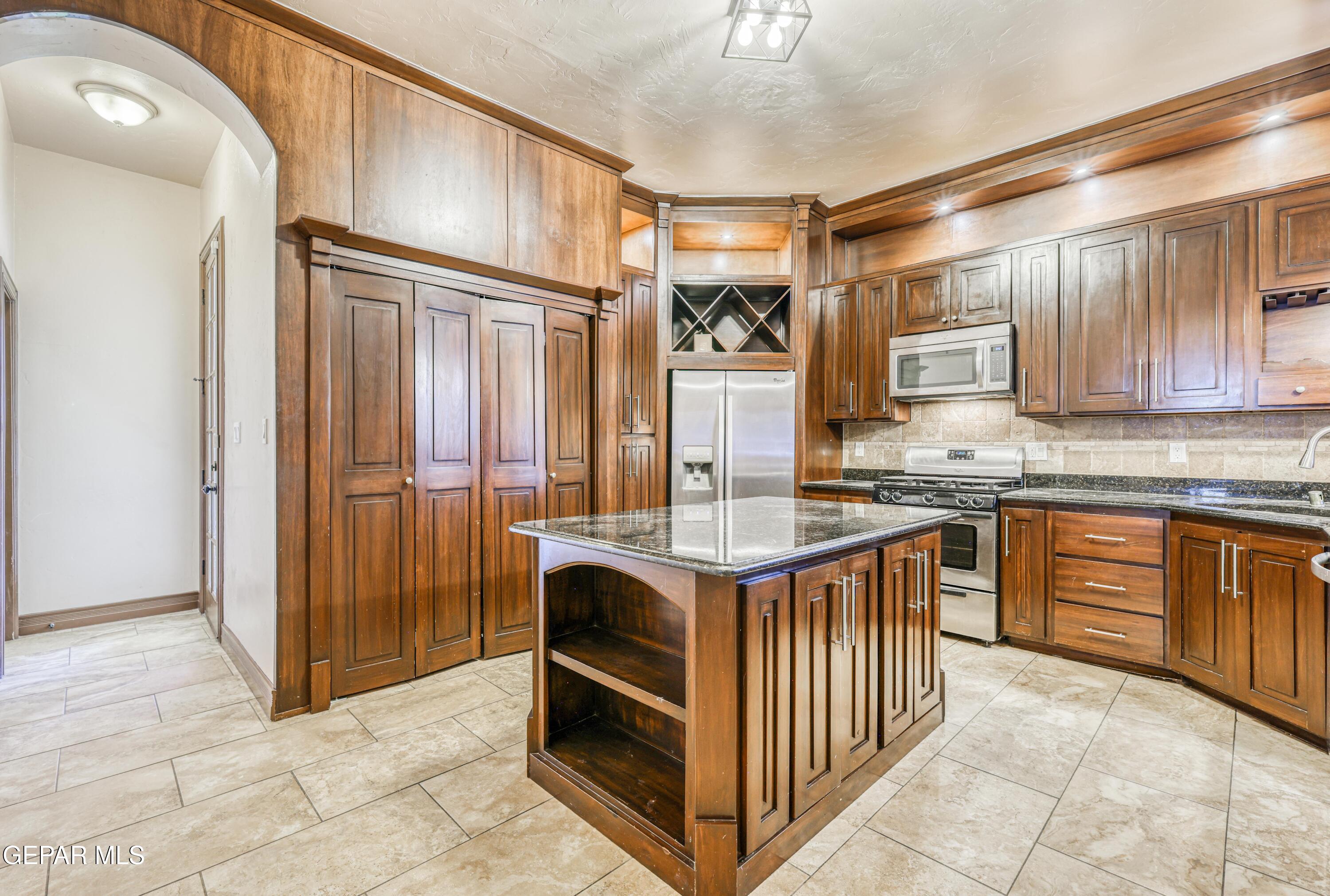 Kitchen with extensive wood cabinetry, a granite-topped island, stainless appliances, and a built-in wine rack.
