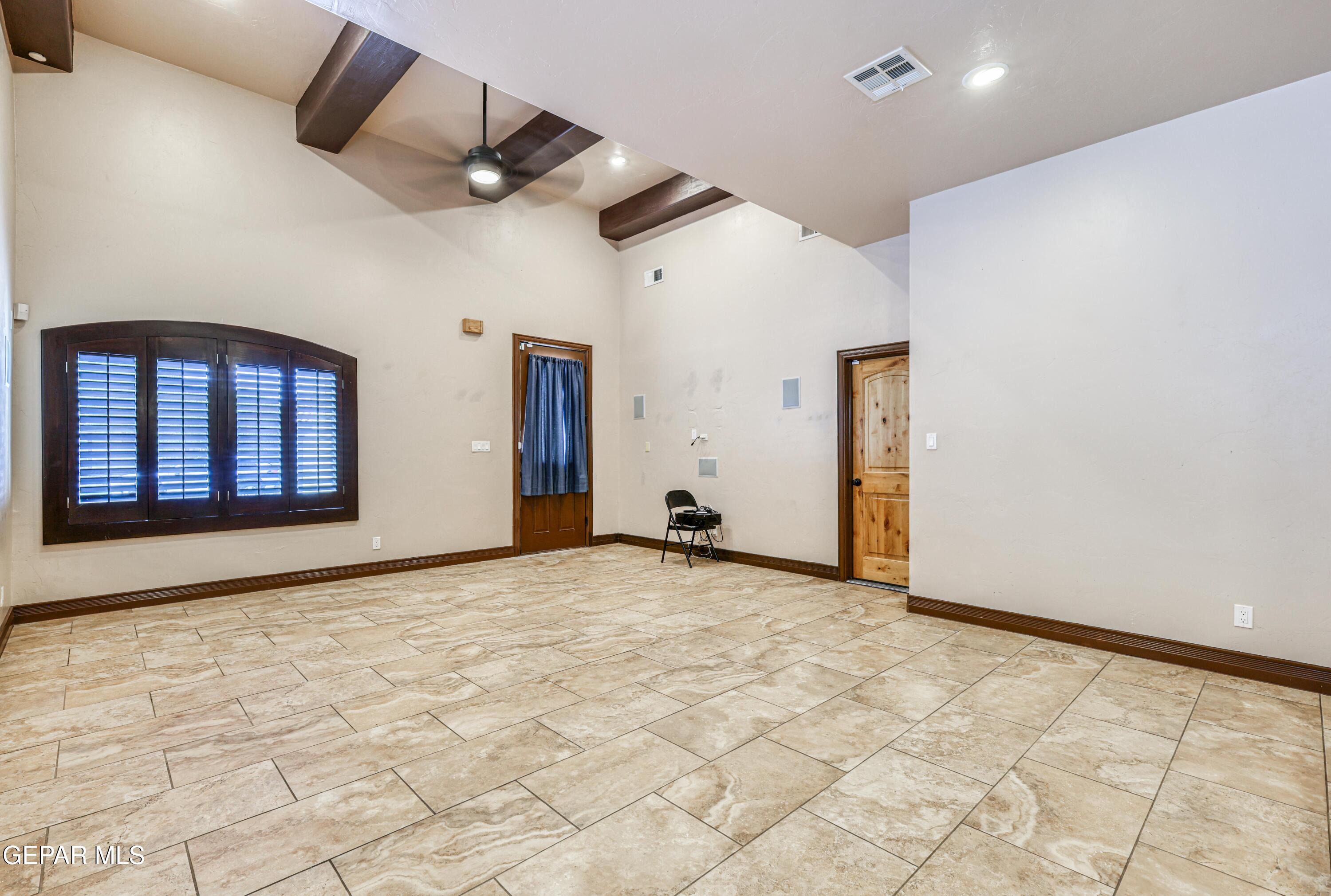 Empty tiled room with exposed ceiling beams, a shuttered window, and two wooden doors.