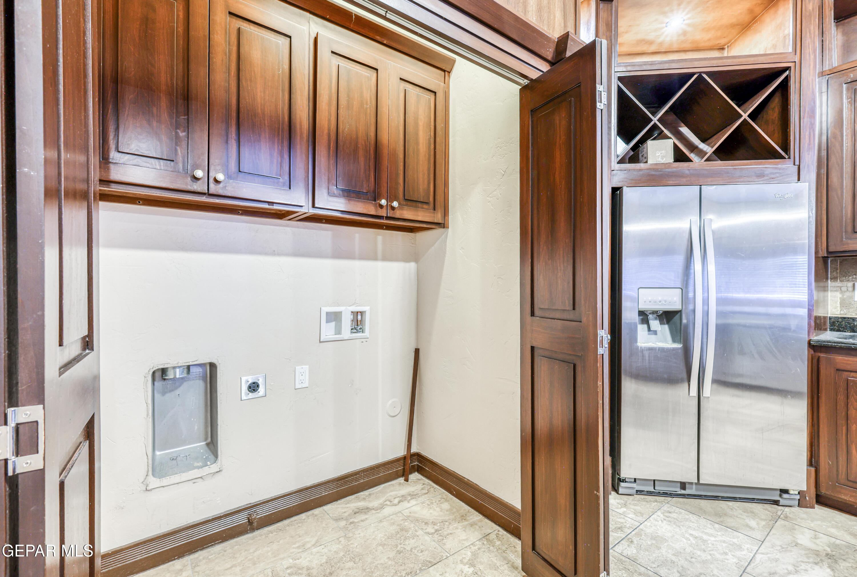 Kitchen with dark wood cabinets, stainless steel refrigerator, and built-in wine rack beside laundry hookups.