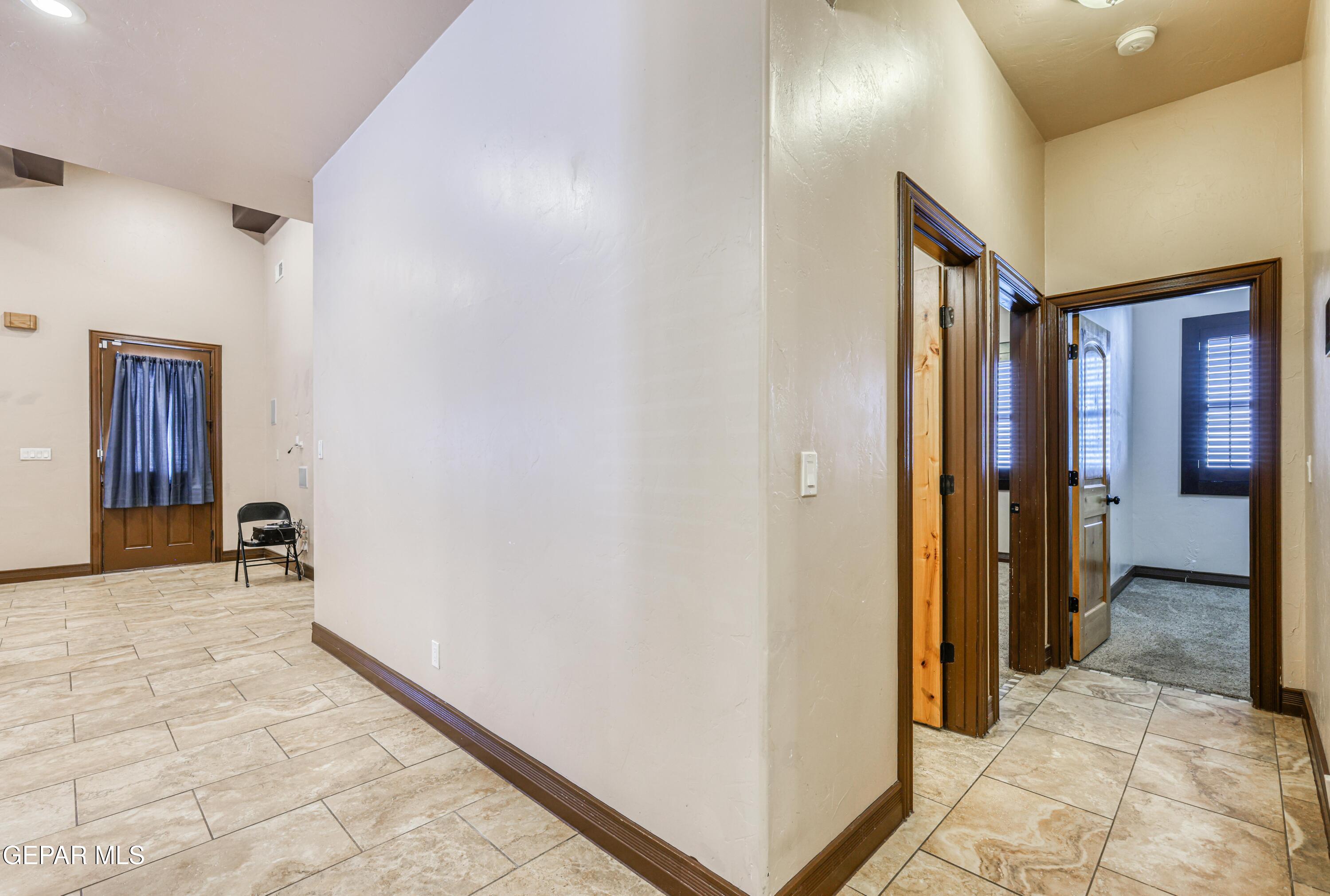 Hallway with tan tile floors, dark wood doorways, and a curtained door.