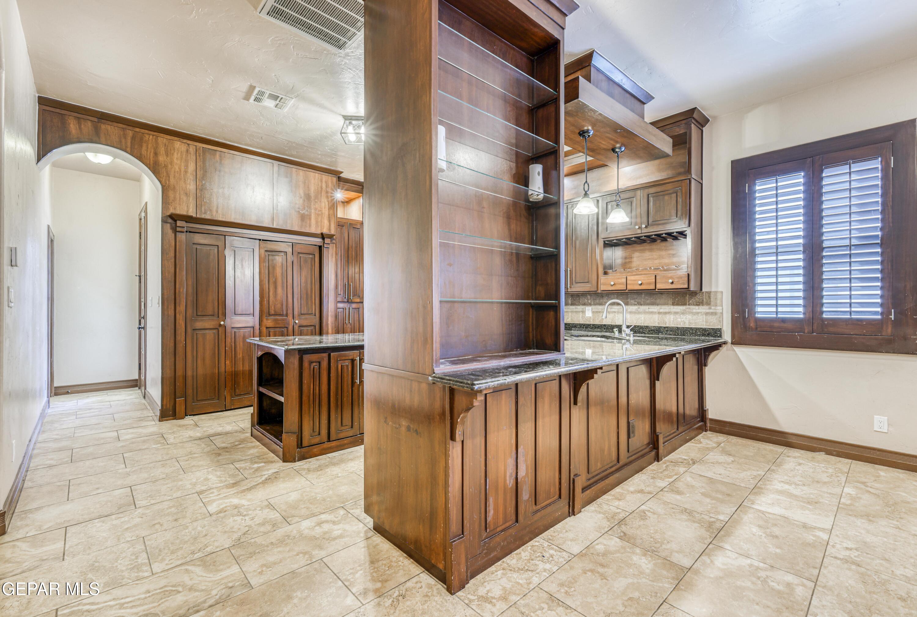 Kitchen with dark wood cabinetry, a large peninsula with open shelving, granite counters, and shuttered window.